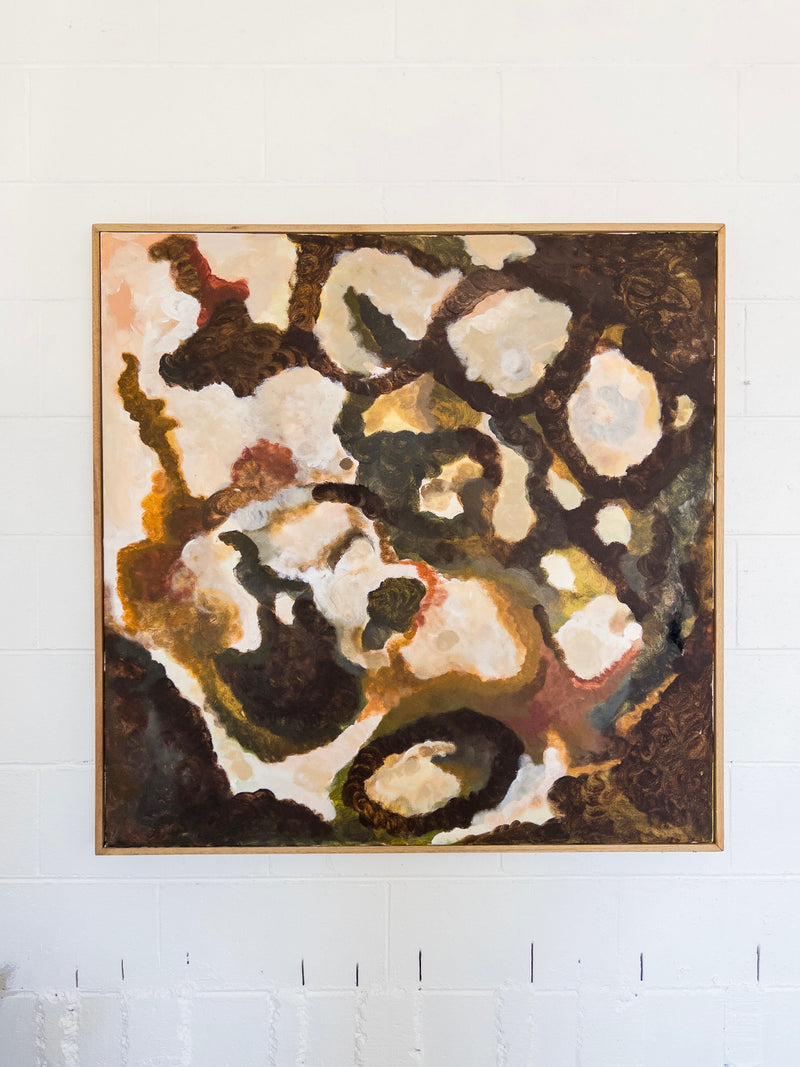 The "That Which Remains" painting by Natasha France is a square abstract canvas artwork that features a blend of earth tones including brown, green, and white. Swirling patterns and textured layers add depth and movement to this mixed media piece. It is framed in simple Tasmanian Oak and mounted on a white wall.