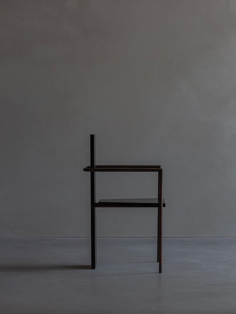 The Bicci de' Medici Jonas Bohlin CONCRETE chair, with its geometric and minimalist design, sits against a bare gray wall. Its unique angular structure of horizontal and vertical lines offers a modern, artistic look under soft, subtle lighting.