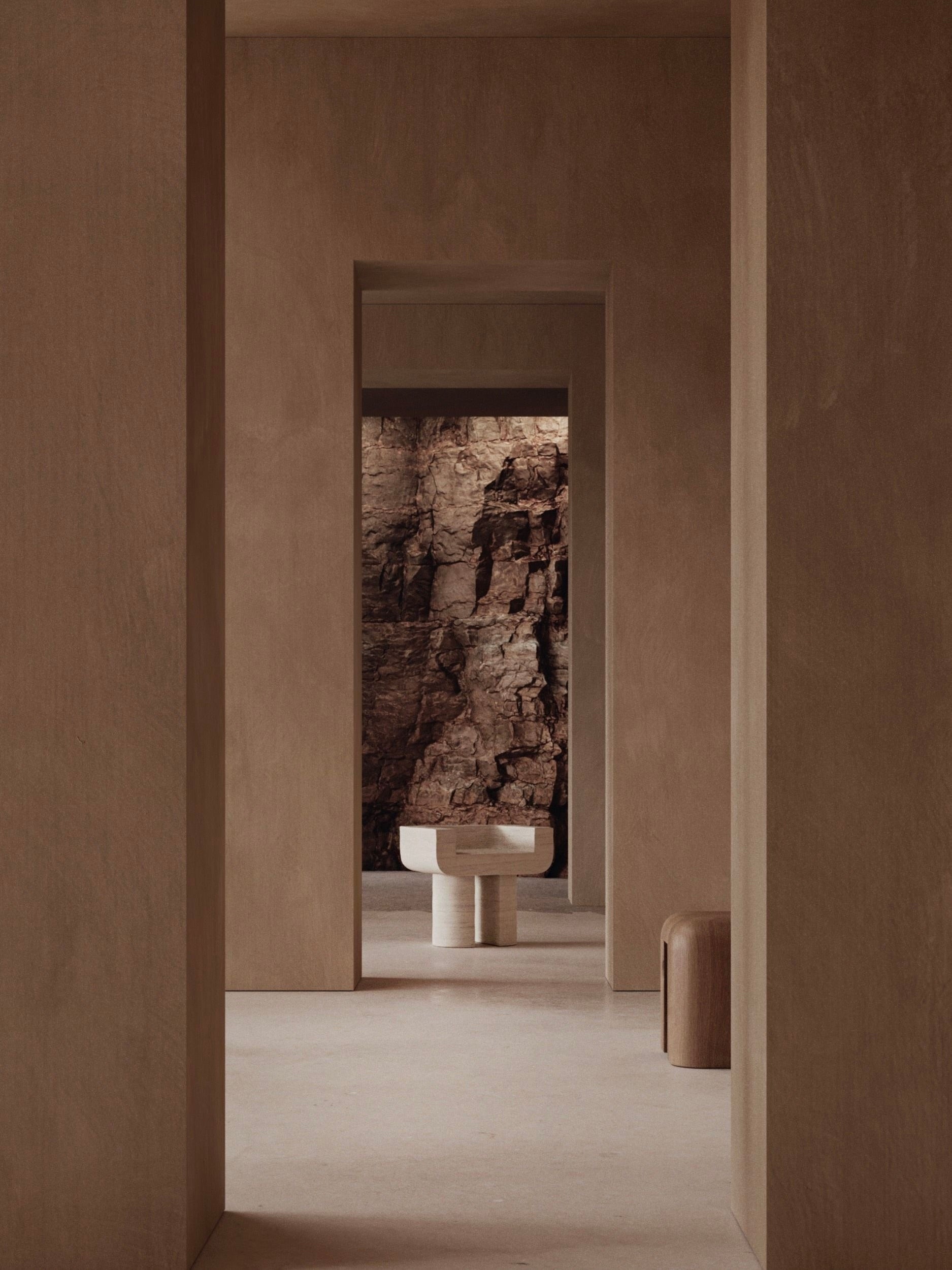 A minimalistic interior showcases a narrow hallway with neutral walls. A small round table and Monolith's M_001 Chair, with its throne-like design, stand at the end. The chair and a section of textured stone wall introduce an elegant, natural touch to the scene.
