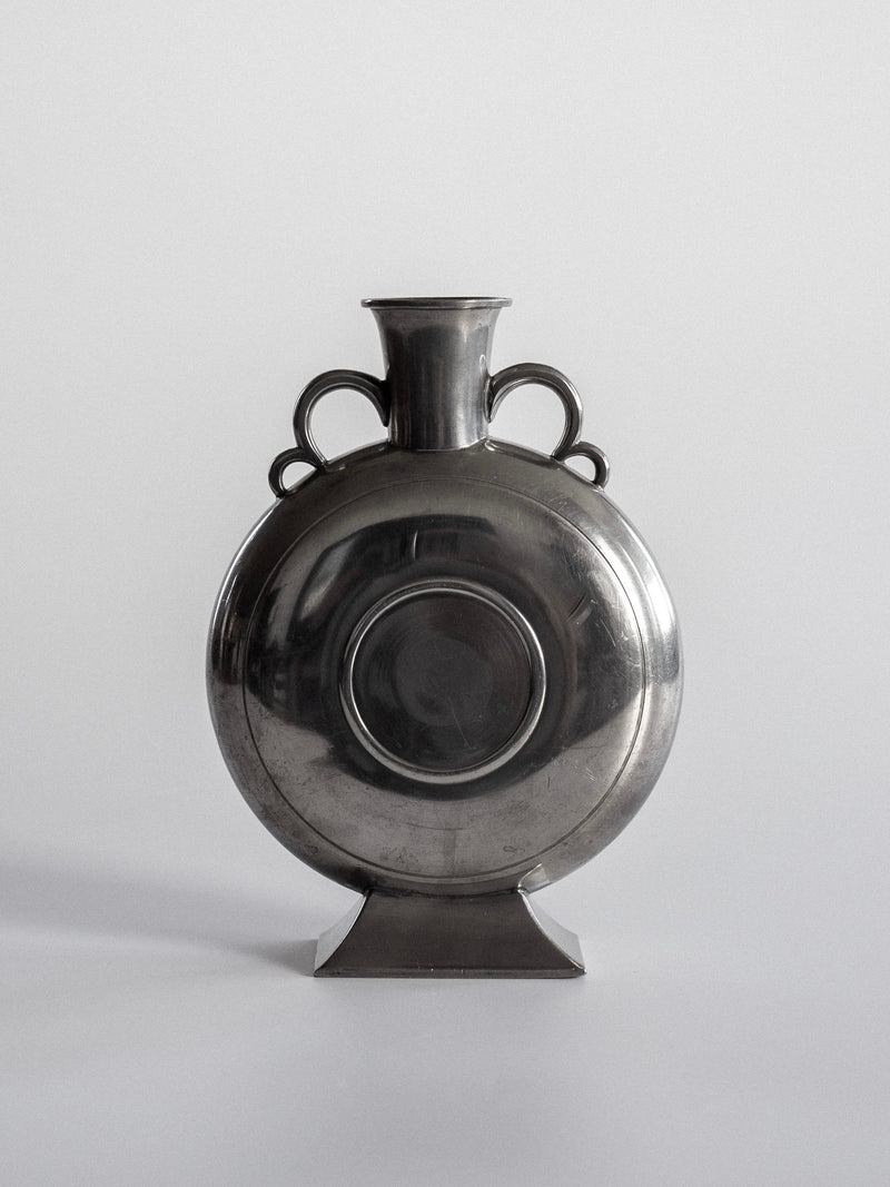 A round Art Deco Pewter Vase by Spigel features a narrow neck, two curved handles, and a flat, square base. Its smooth and reflective surface showcases Scandinavian craftsmanship against a plain gray background.