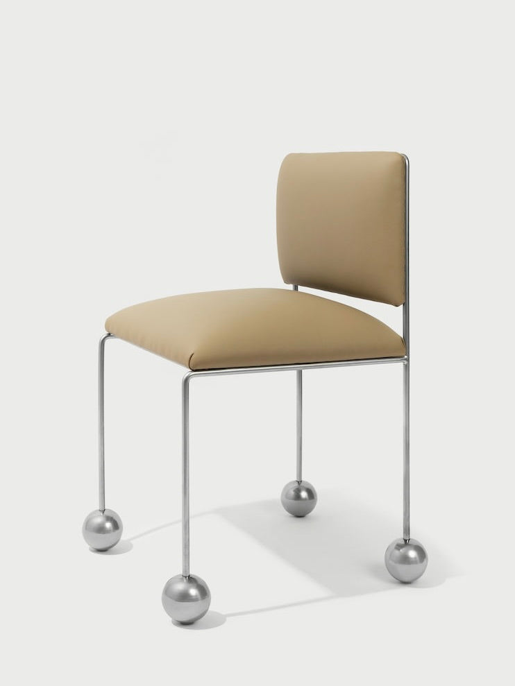 Introducing the 'Ball Foot' Chair by Panorammma, a modern masterpiece with a beige vegan textile cushioned seat. Its minimalist metal frame is accentuated by unique spherical feet, offering an elegant look against a light backdrop.