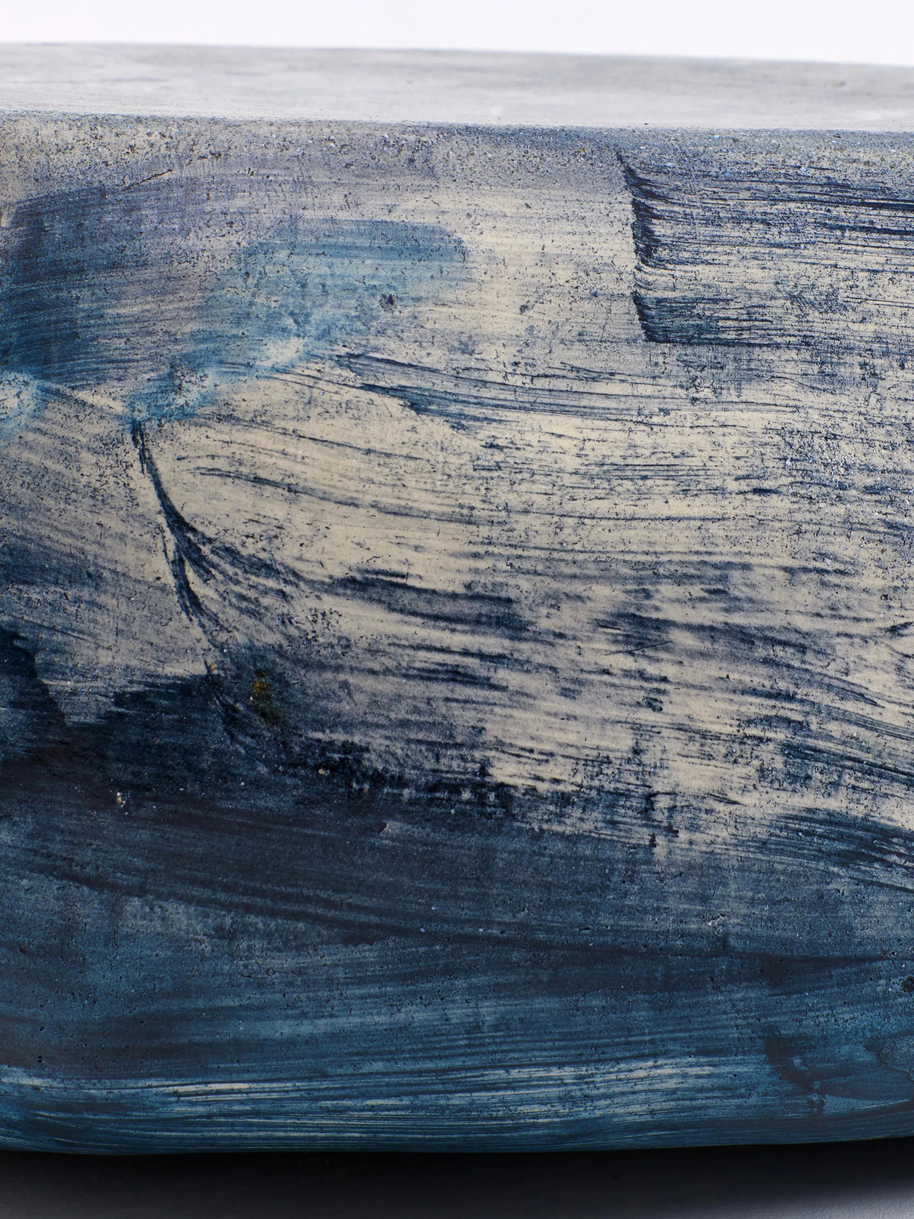 A close-up of the Brushed Blue Ceramic Coffee Table from Project 213A reveals a heavily textured surface painted in shades of blue and white. The rough and varied brush strokes give it the appearance of an abstract or impressionistic work of art, almost like a piece of painted concrete or stone. Its bespoke dimensions add to its unique charm.