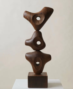 Abstract wooden sculpture with three interlocking organic shapes, displayed on a wooden base.