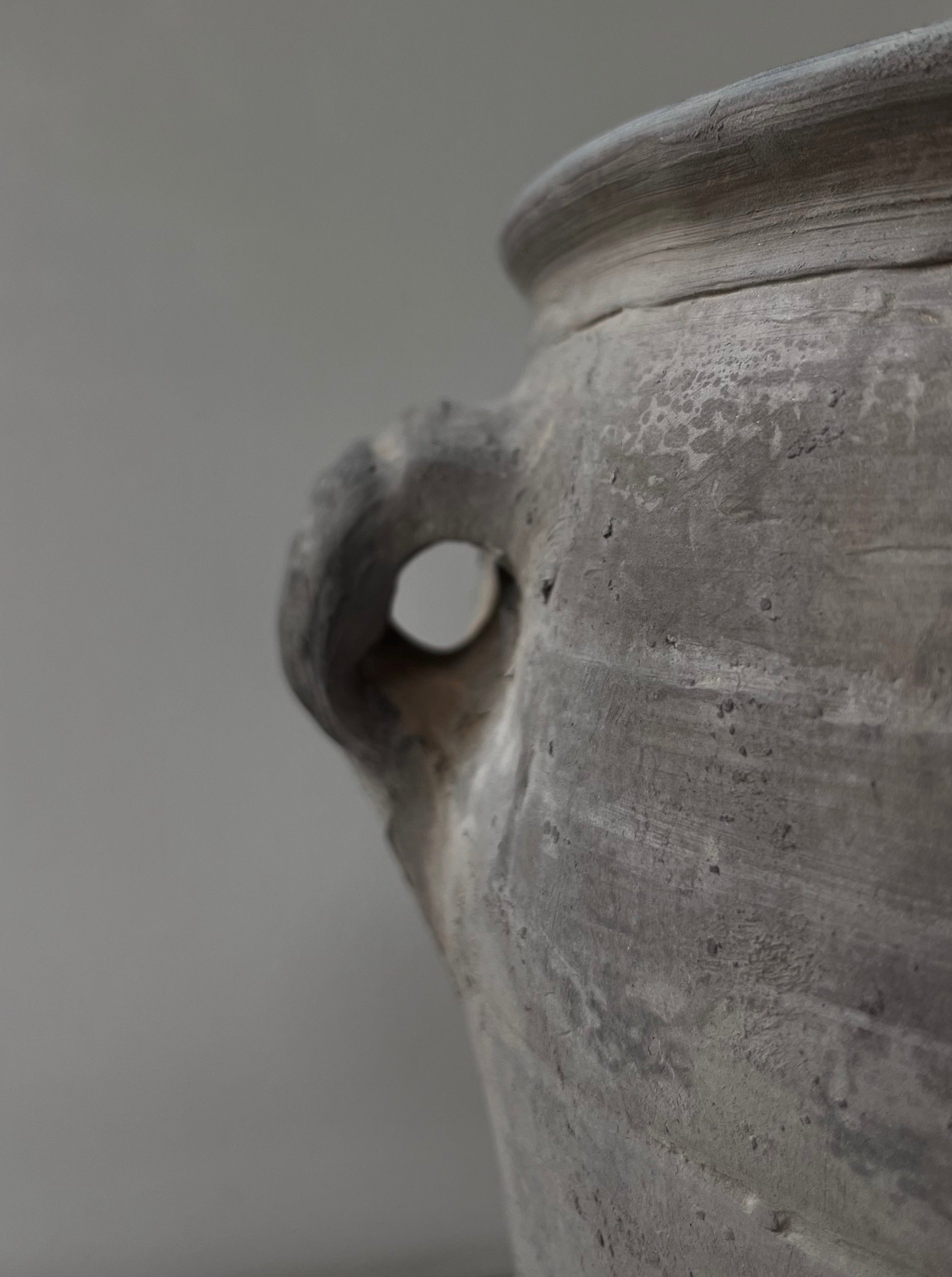 Close-up of an aged, textured Médecine antique earthenware lamp, focusing on the handle and the opening detail, against a soft gray background.