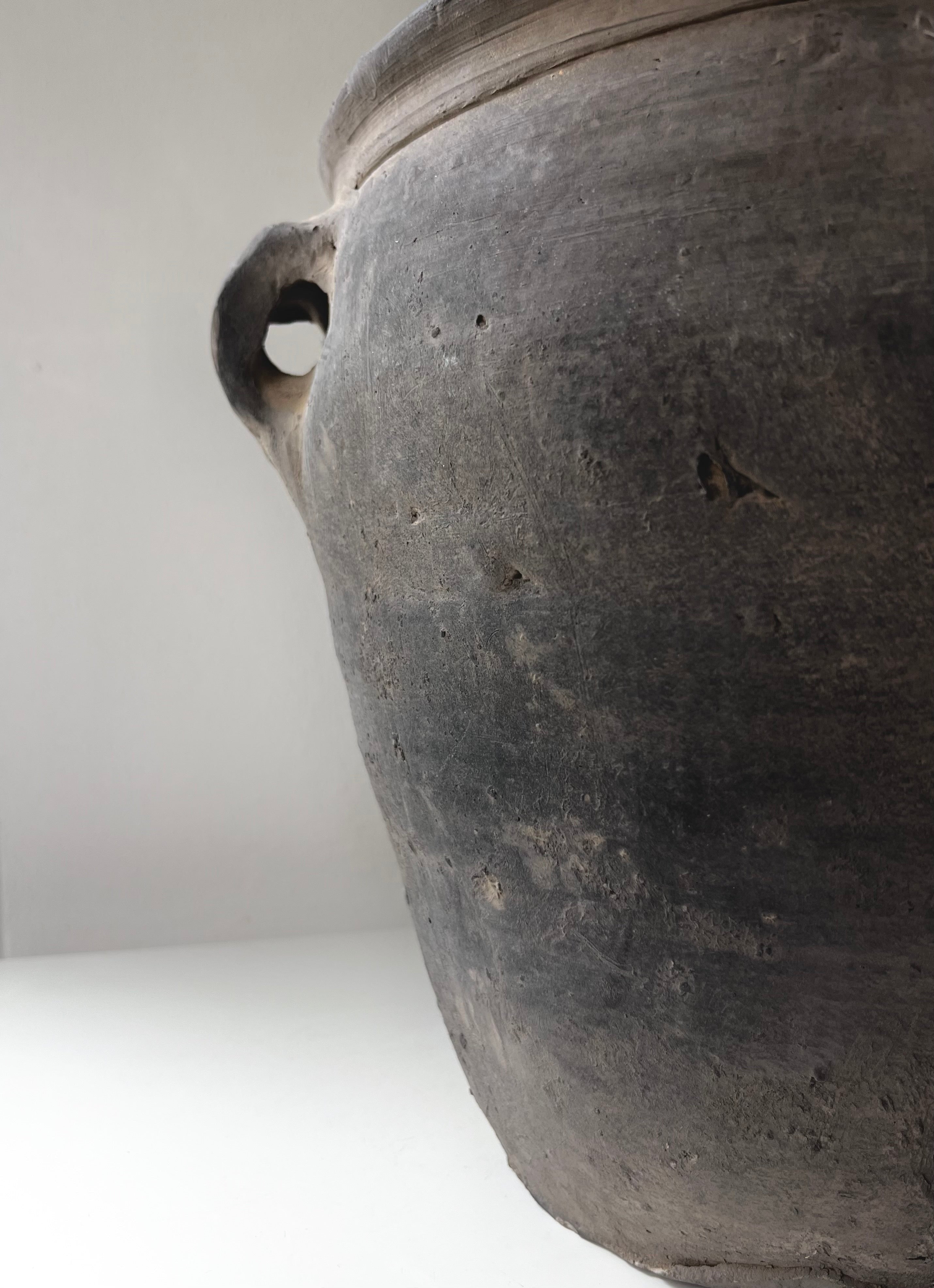 Close-up of a Médecine antique earthenware lamp with a handle, showing textured surface and small holes, against a plain light background.