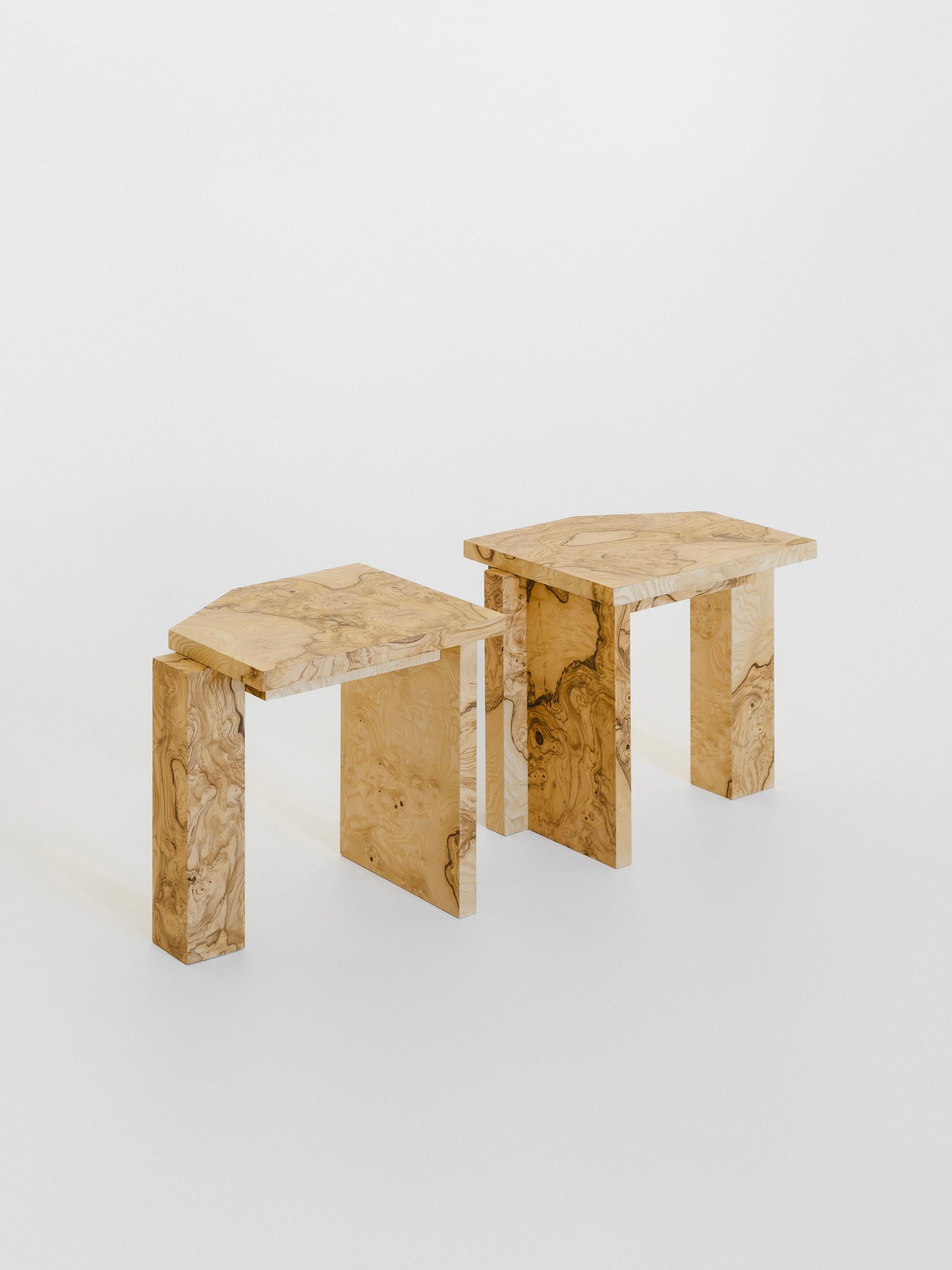 Two abstract wooden tables from the exclusive Edition 8 + 2 A.P., featuring unique geometric shapes and swirling grain patterns on a white background, boast angular lines and a minimalist aesthetic. Alongside the SSS01W Stool by sashaxsasha, these pieces emerge as modern design icons.