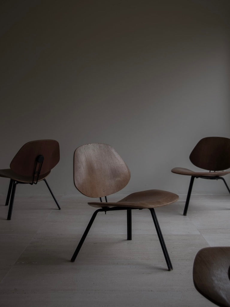 Four Osvaldo Borsani - P31 wooden chairs by Bicci de' Medici, featuring metal legs and Italian Mid-Century design, are set on light tiles against a plain wall. The minimalistic setting and soft lighting create a calm and simple atmosphere.