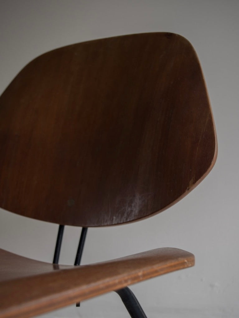 A close-up of the Italian Mid-Century Osvaldo Borsani - P31 brown wooden chair by Bicci de' Medici highlights its backrest and seat, with black metal legs visible against a plain light gray wall, capturing the essence of Borsani's design for Tecno.