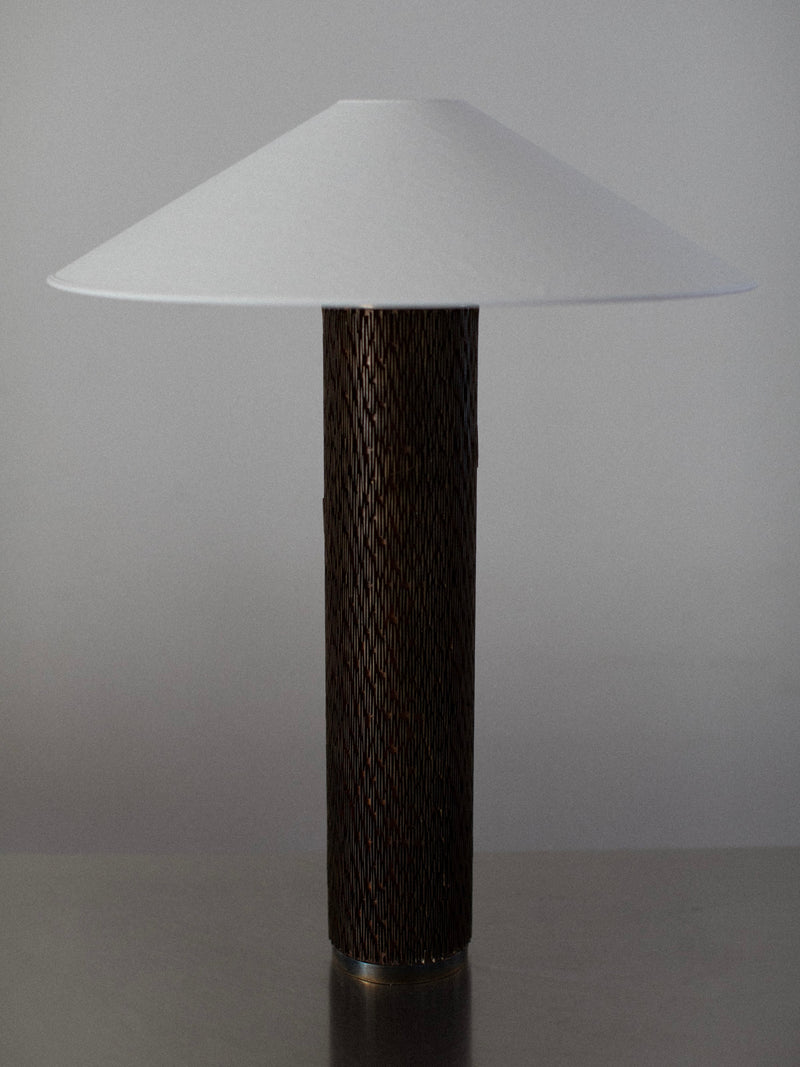 The Brutalist Floor Lamp by Out For Lunch features a sleek, modern design with a wide, white conical shade and a cylindrical wooden base. It is elegantly placed on a plain surface against a neutral background.