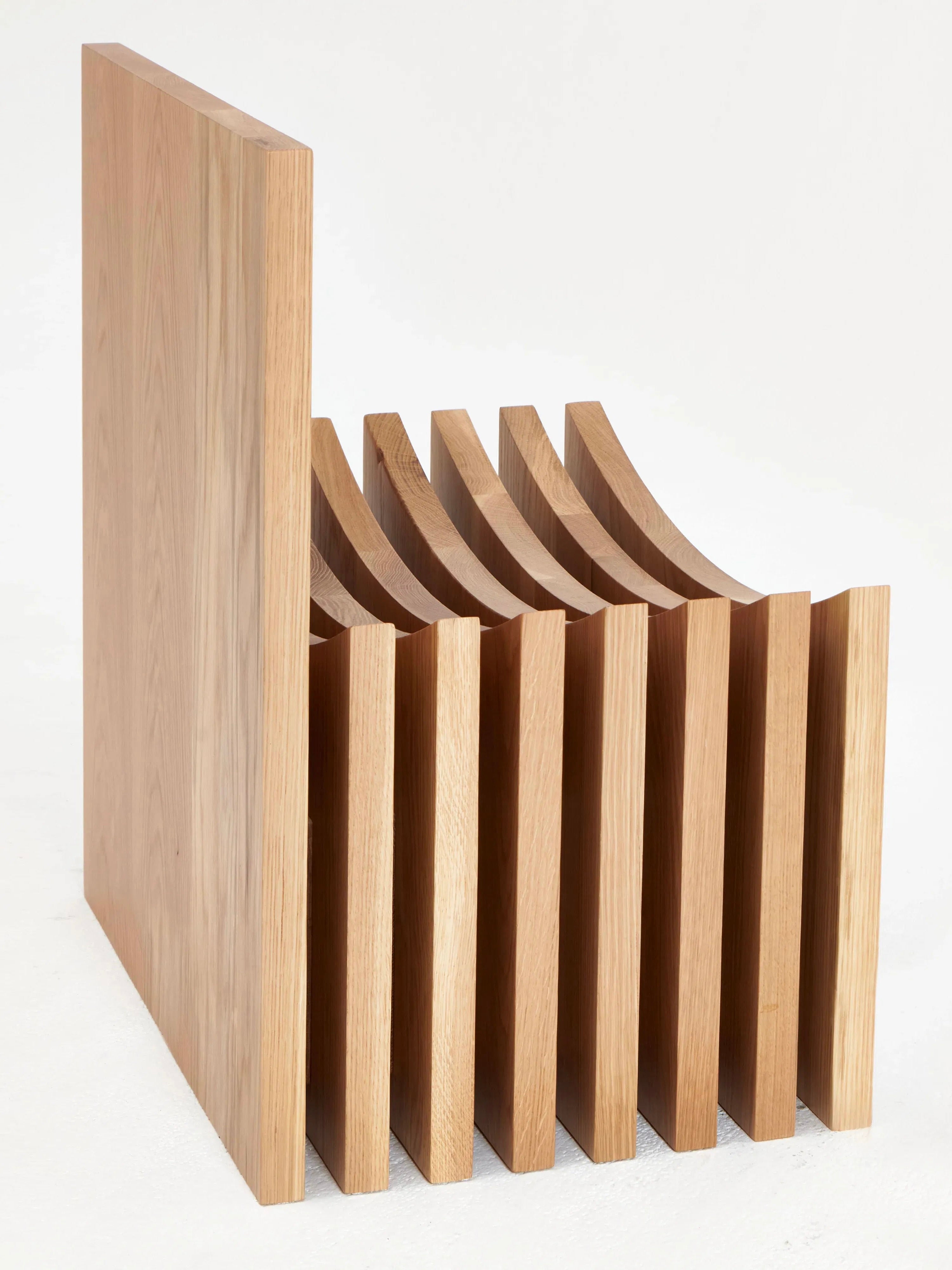 The Melides Chair by Project 213A is a modern wooden piece with a unique design, featuring multiple vertical slats for the seat and backrest, creating a visually striking and sculptural look. Hand-crafted from solid oak, its smooth finish and natural grain give the chair a warm and organic appearance.