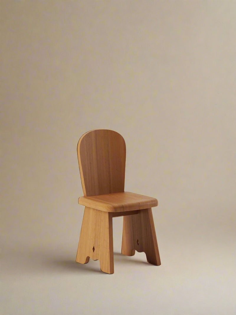 The Rambling Chair by Lemon, crafted in honey French oak wood, rests against a plain beige backdrop. Its minimalist design and smooth natural texture perfectly complement contemporary living, radiating simple charm as it is gracefully centered in the image.