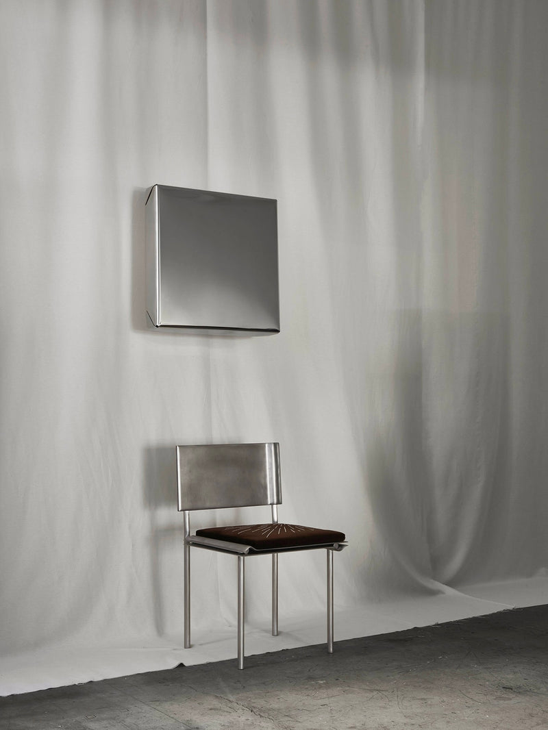 Modern square mirror with metallic frame mounted above minimalist steel chair