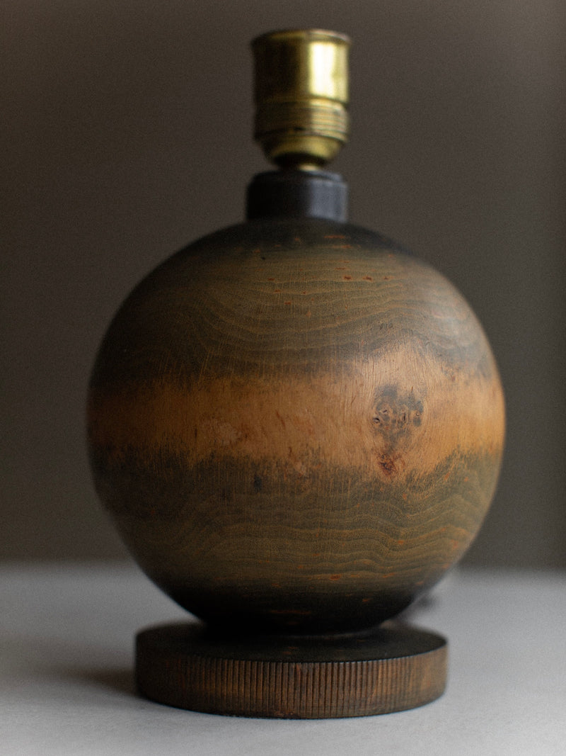 The Out For Lunch 1920's Globe Lamp, featuring a dark wooden spherical base with lighter, natural grain patterns and an impeccable wood finish, is showcased against a neutral background. Its brass light socket adds a touch of vintage decor, while the lamp rests elegantly on its circular wooden base.