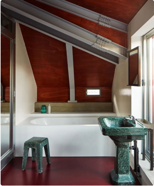 Modern bathroom with a green marble sink, freestanding bathtub, and red flooring, set against a backdrop of wood-paneled walls and industrial design elements.