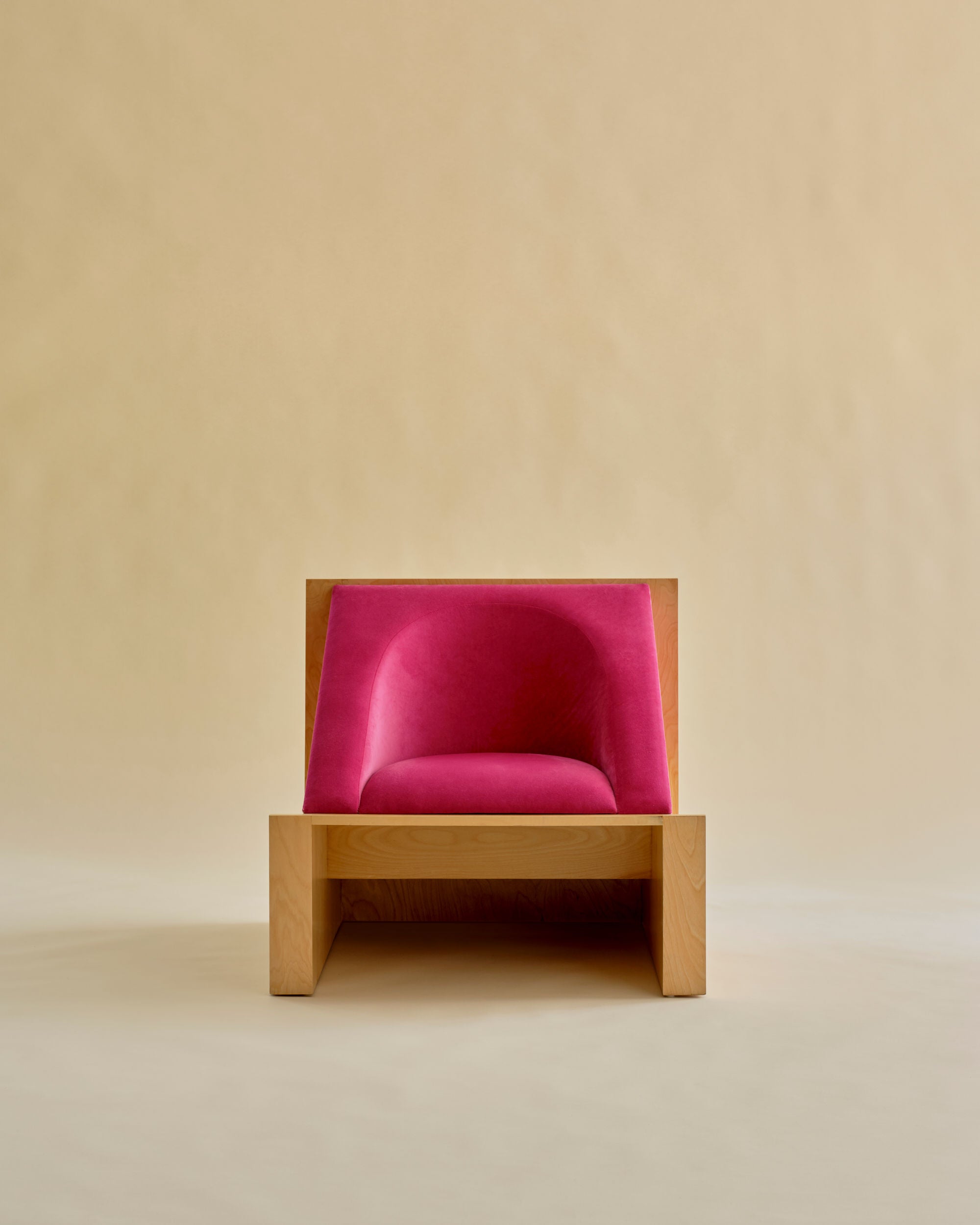 Known Work presents the 'Perceptions' Armchair: a modern masterpiece featuring a minimalist light wooden frame and vibrant pink upholstery, combining style with comfort against a serene beige backdrop.