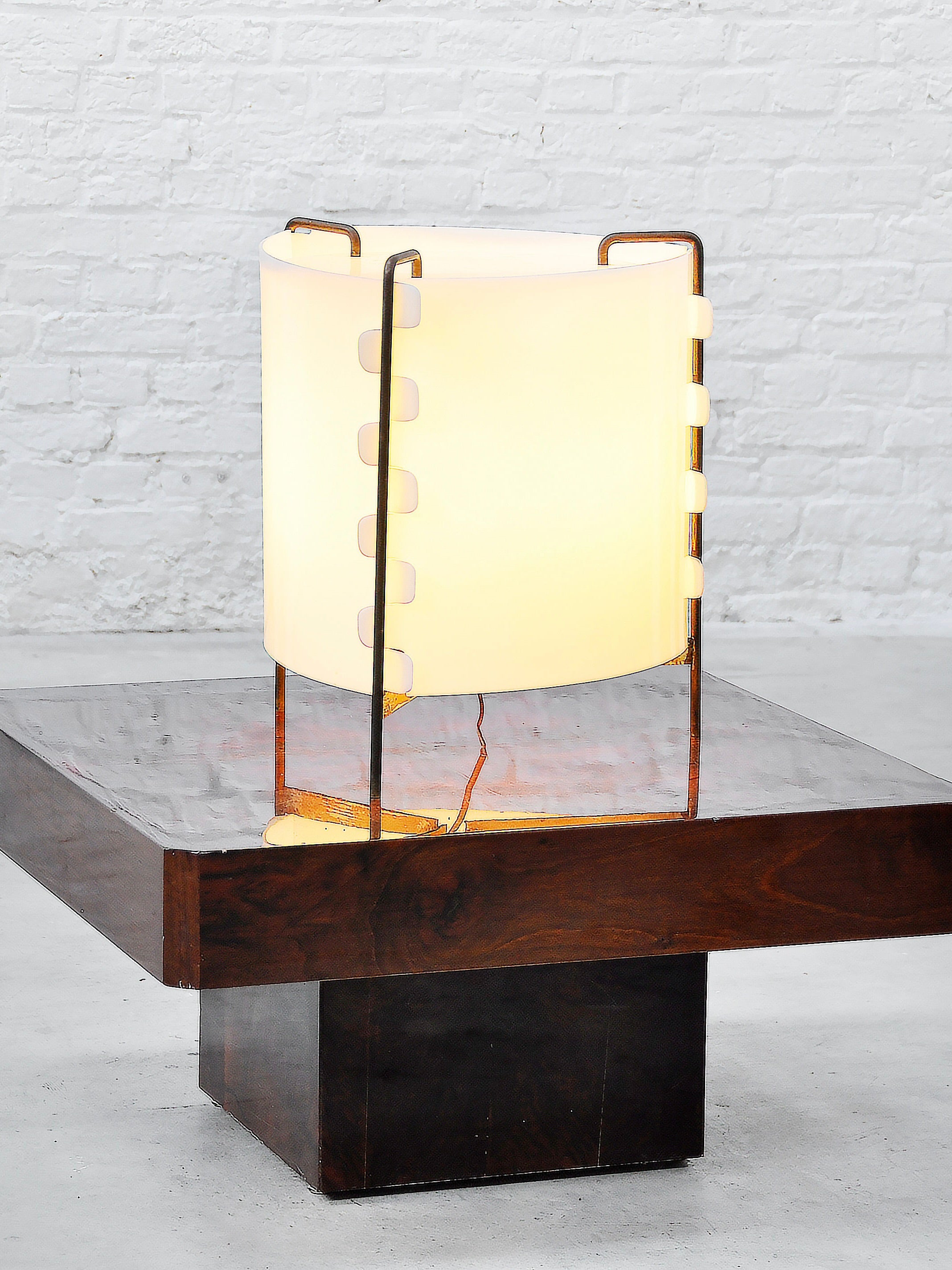 The 'M8 Fanal' lamp by Joseph-André Motte for Huchers-Minvielle, France 1958, from Introverso, recalls mid-century modern style with a frosted glass shade and wooden frame. It gently glows on a polished wooden table against a white brick wall.