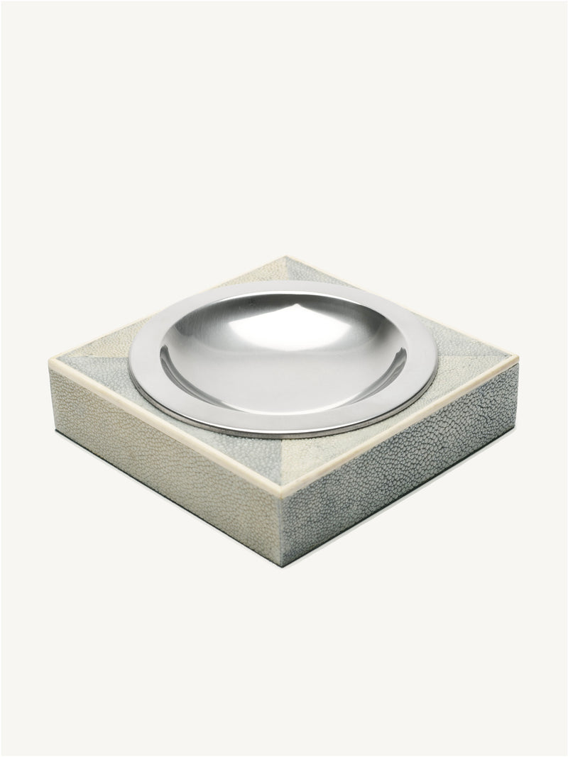 The Shagreen Ashtray by Galerie MLS features a square, textured light surface with a central round, shiny metal dish. Its minimalist, modern design evokes the clean lines of an art deco ashtray.