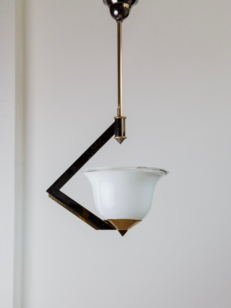 The Vintage Ceiling Lamp Murano Glass by Bottega Jacobs, inspired by retro chandeliers from 1980s Italy, showcases a sleek, angular black metal frame paired with a white glass shade adorned with a pointed brass tip, elegantly suspended from the ceiling against a plain backdrop.