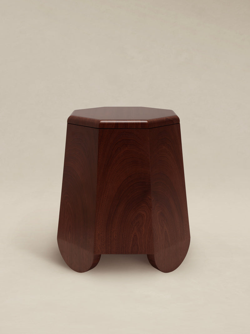The Chatior Side Table by AÈDE Studios features a dark wooden hexagonal top inspired by medieval Russian architecture and has elegantly smooth, curved legs. It stands gracefully against a simple, light-colored background.