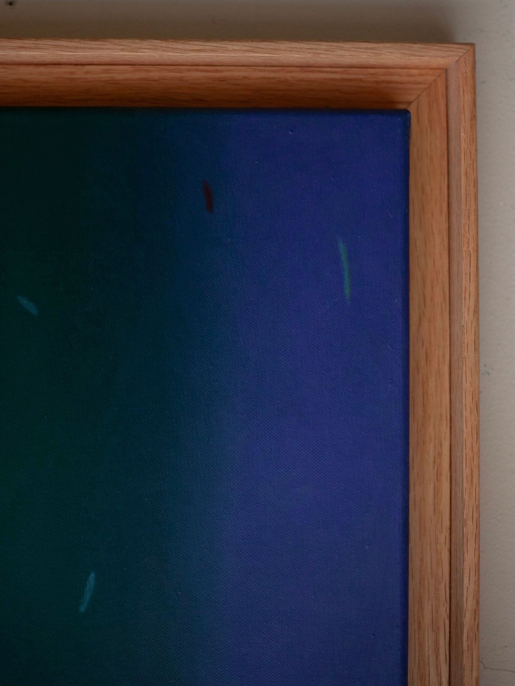 A close-up of "Fade into #2, 2024" by Rebecca von Matérn, displayed in a hard wax oiled oak shadow frame. The painting showcases a gradient of colors ranging from deep green to dark blue, with delicate specks of light tones scattered across its 36x36 cm canvas.