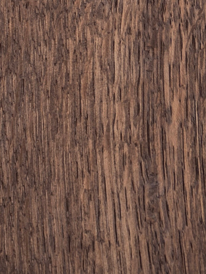 Close-up of the textured brown wood surface on the solid oak Paris Dining Table by Obstacles, highlighting its visible grain patterns and natural imperfections.