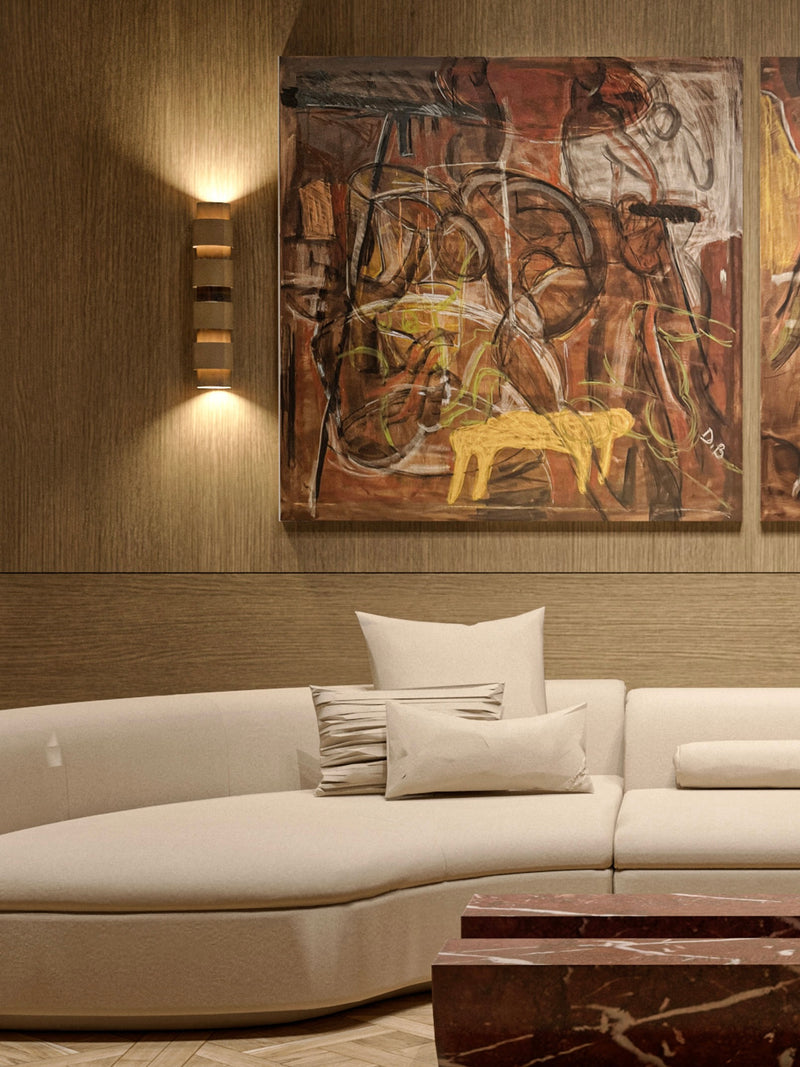 A modern living room showcases a curved white sofa accented with cushions. Above, the 'Hidden Narratives' vol. 01 painting by Dovile Bernotaite, featuring abstract forms in earthy tones, hangs on a textured wall illuminated by a sleek wall light. A reddish-brown marble table injects bold color contrasts and is partially visible in the foreground.