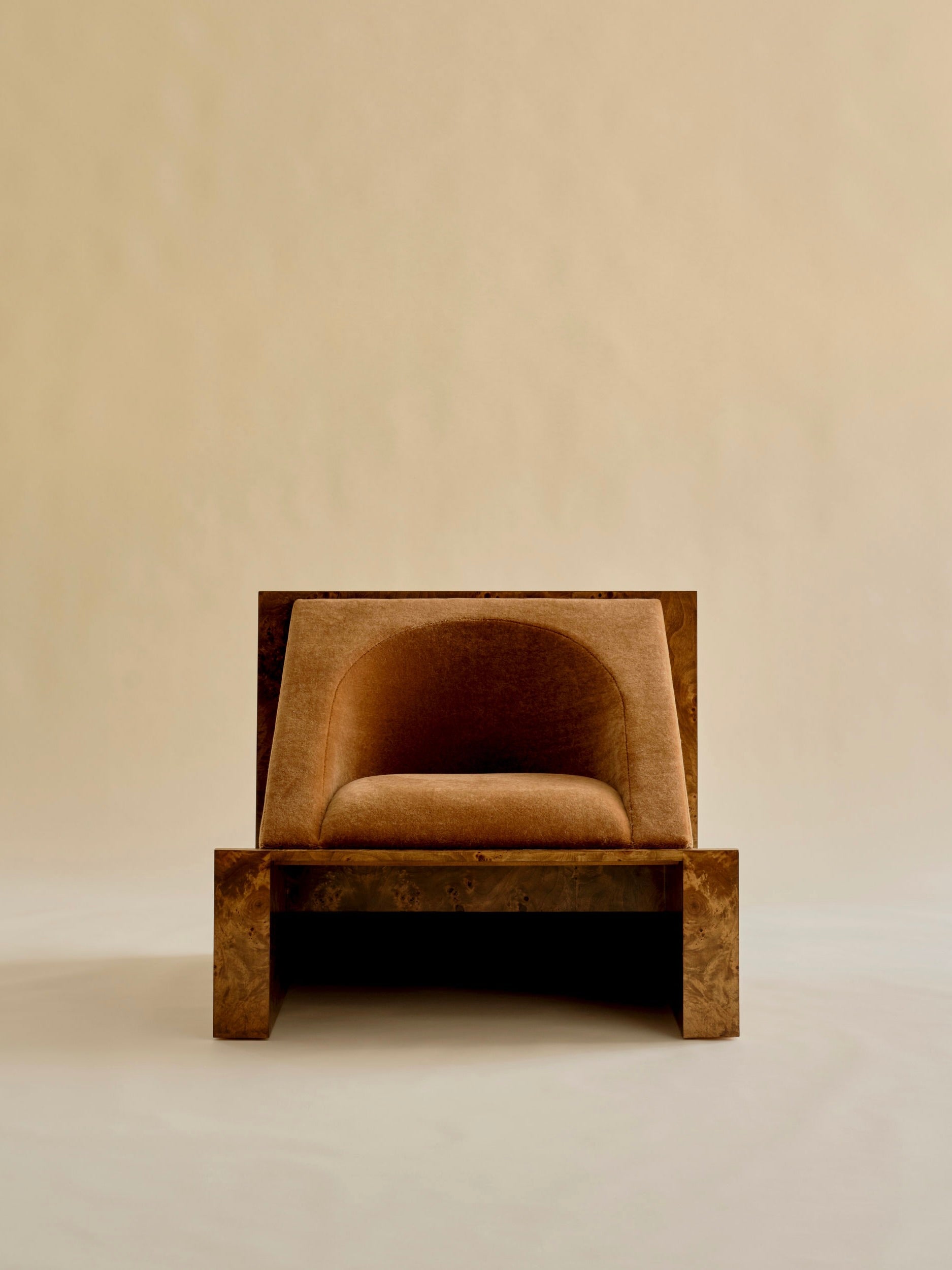 The 'Perceptions' Armchair by Known Work is a minimalist design with a rectangular wooden frame and plush, rounded brown upholstery, set against a plain beige background.