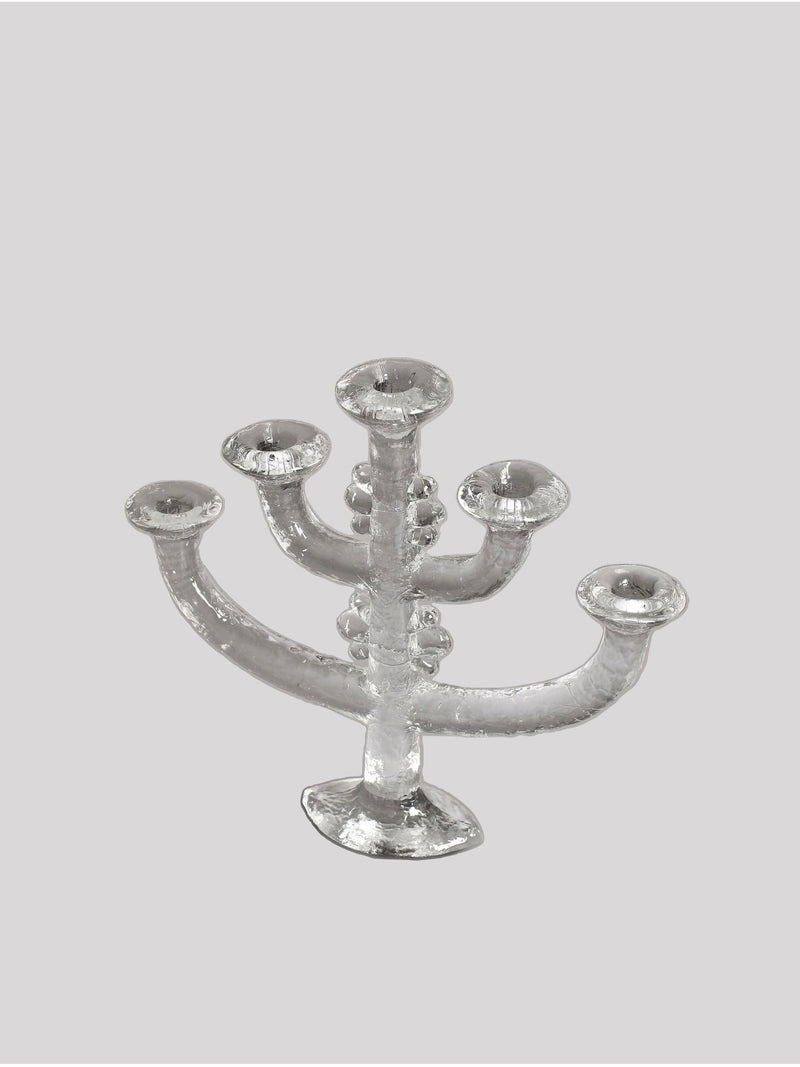 A transparent, intricately designed Large Glass Candlestick by Staffan Gellerstedt from RELIC LONDON features five branches, each capable of holding a single candle. With its textured finish adding a delicate and elegant touch, this piece is reminiscent of Pukebergs Glasbruk craftsmanship and brings vintage charm against a plain light-gray background.