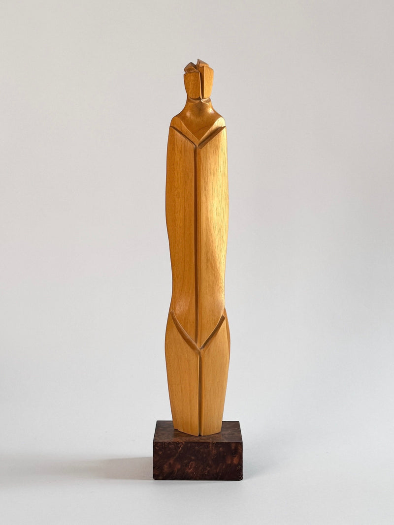 Crafted by Figuresdesign, this Light Wood Sculpture by Pierre Dedieu features a minimalist human figure with angular, abstract shapes and a smooth finish. It stands on a dark rectangular base against a neutral background.