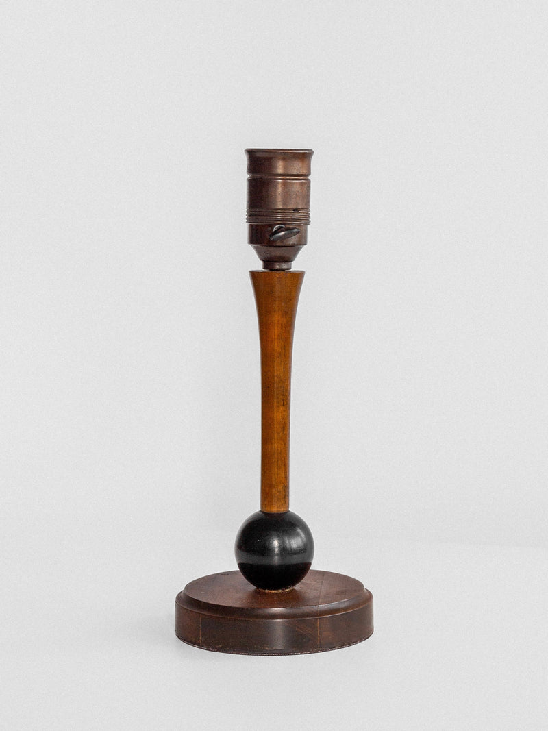 Introducing the Wooden Art Deco Table Lamp by Spigel, a 1930s Sweden-inspired piece featuring a vintage wooden base with a round black sphere near the bottom. The design includes a circular, flat wooden platform and an elegantly tapering column that extends upward to a metal socket. Perfectly showcased against a plain white background.