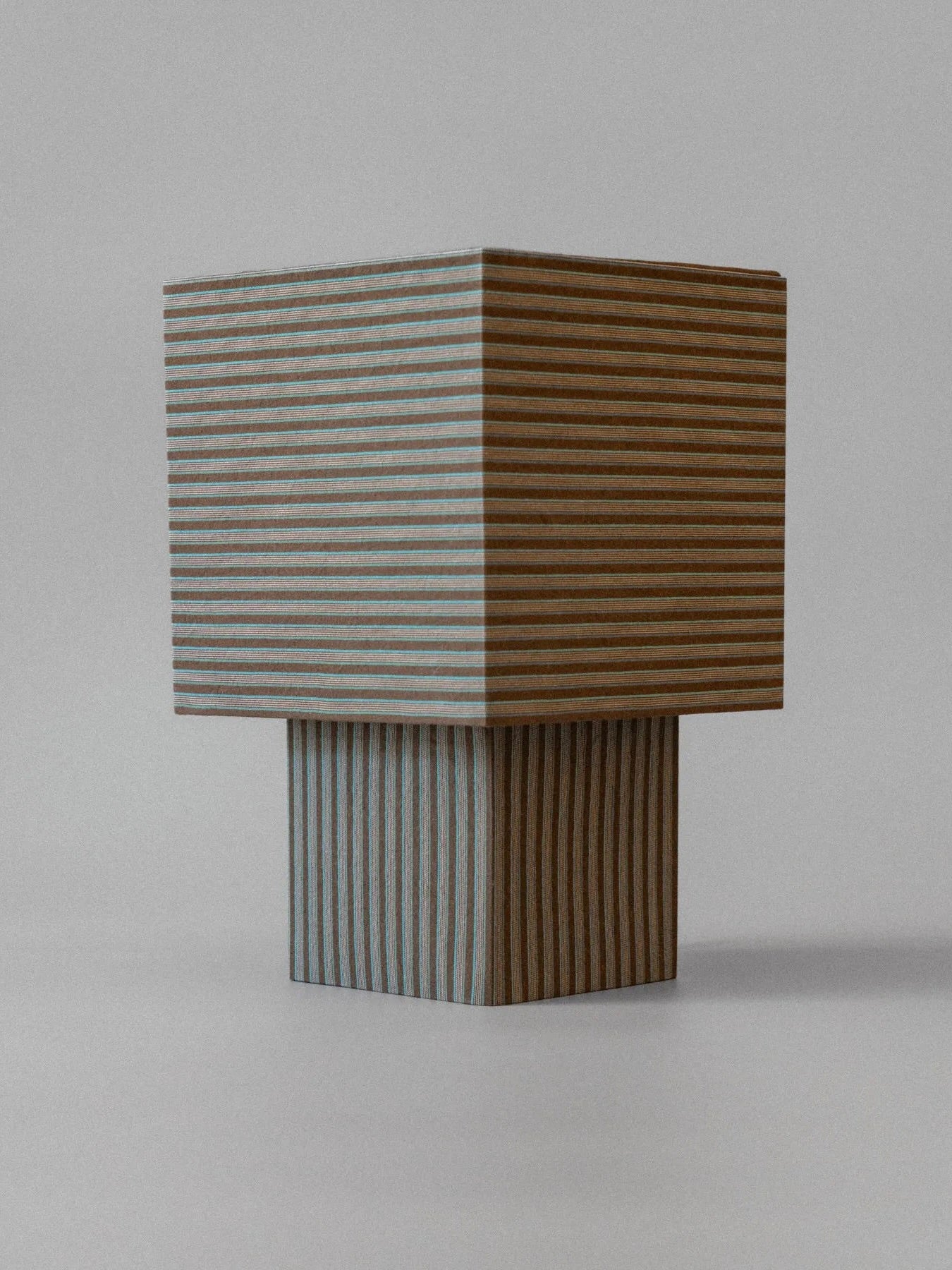 The "La Petite Boîte" - Brown Stripes Table Lamp by mattina moderna features a handcrafted wooden design with vertical stripes, set against a plain background. Its top section is larger and cube-shaped, while the base forms a rectangular design. The consistent stripe pattern radiates modern minimalism and embodies sustainability through its timeless approach.