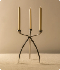 Sleek modern metal candle holder with three long white candles on a minimalist table.