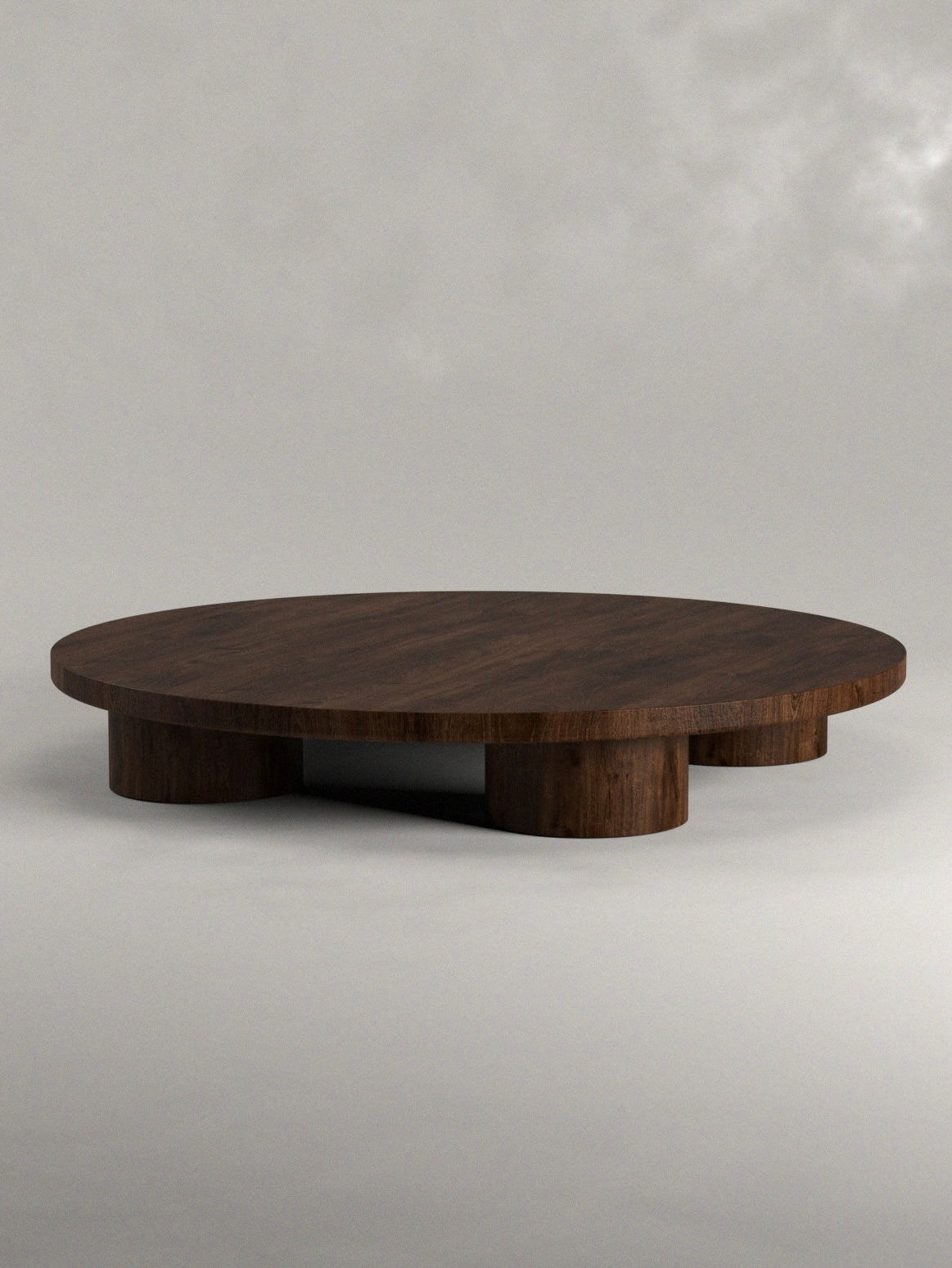 The Siete Studio Totem Coffee Table is a modern piece with a round top and four cylindrical legs. Handcrafted from solid walnut, it boasts a smooth dark wood finish that contrasts beautifully against its neutral gray background.