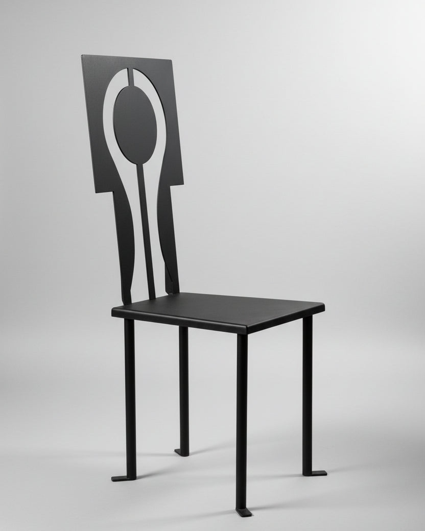 The Luna Chair in Iron and Black Powder Coat by Animate Objects features a geometric backrest with a circular cutout, set on a polished brown floor against a plain light wall. This handcrafted piece is made in Istanbul.