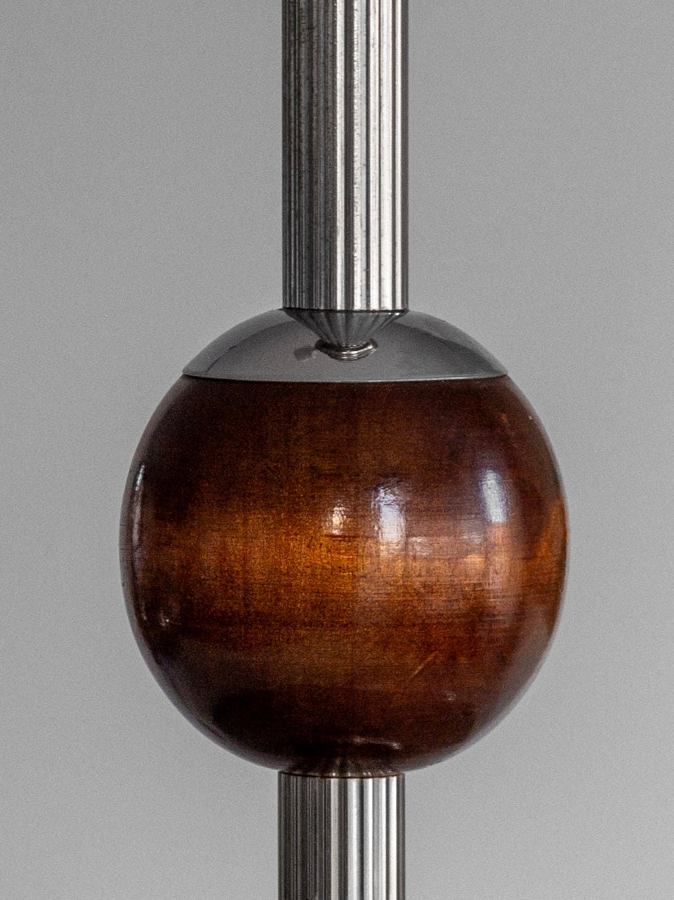 The *Spigel* Wood & Chrome Table Lamp from the 1930s showcases an Art Deco design with a wooden sphere gracefully nestled between two vertical, ribbed chrome rods. The sphere's rich brown finish beautifully contrasts with the sleek, reflective metallic surfaces of the rods, echoing the craftsmanship of 1930s Sweden.