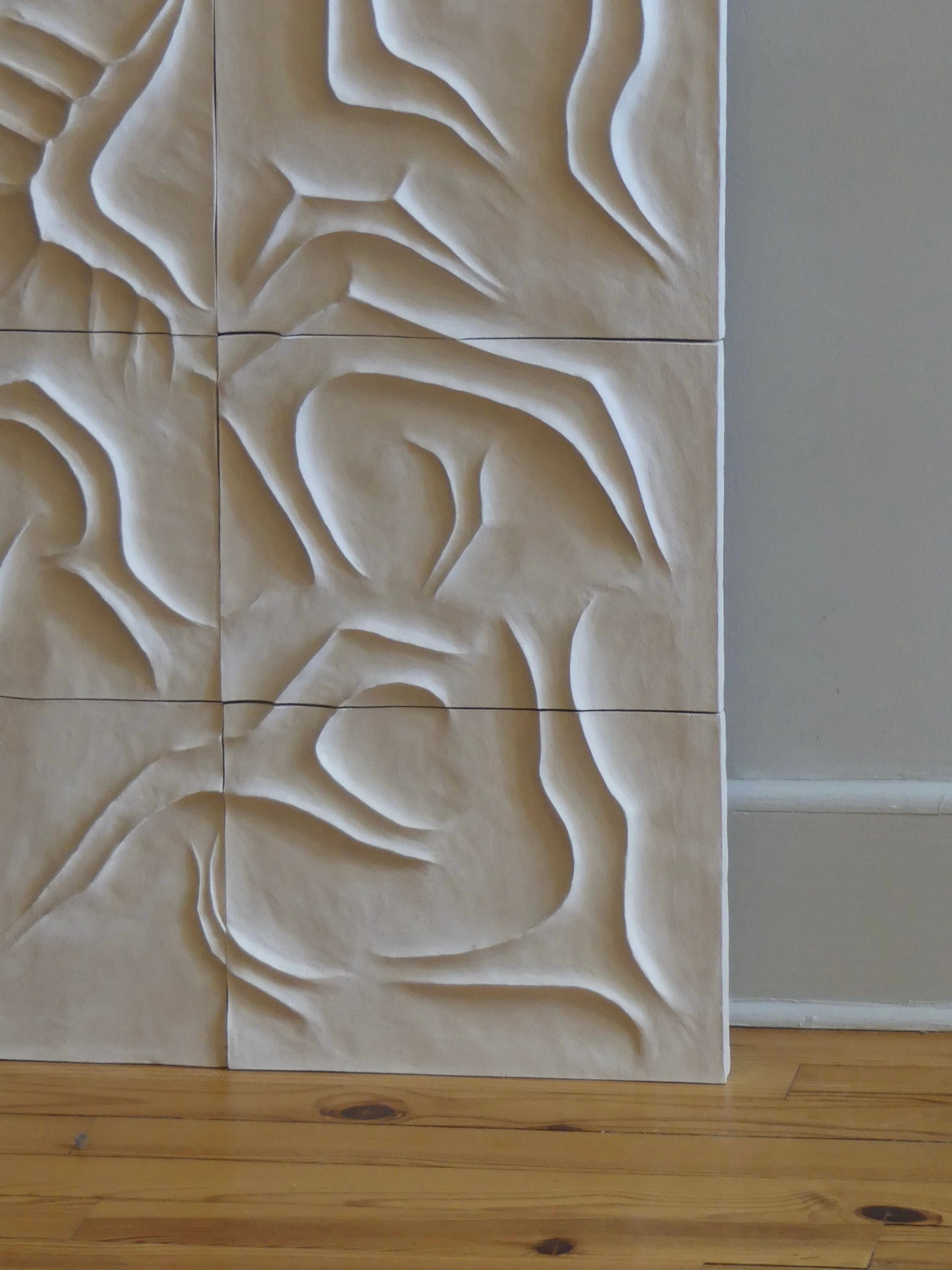 The wall features six panels of carved, abstract bas-relief designs with flowing curved lines. The light beige panels create a striking contrast against the wooden floor and plain light-colored wall, echoing the natural elegance of Franck Scala's "Scala Dei Turchi - Wall Sculpture.