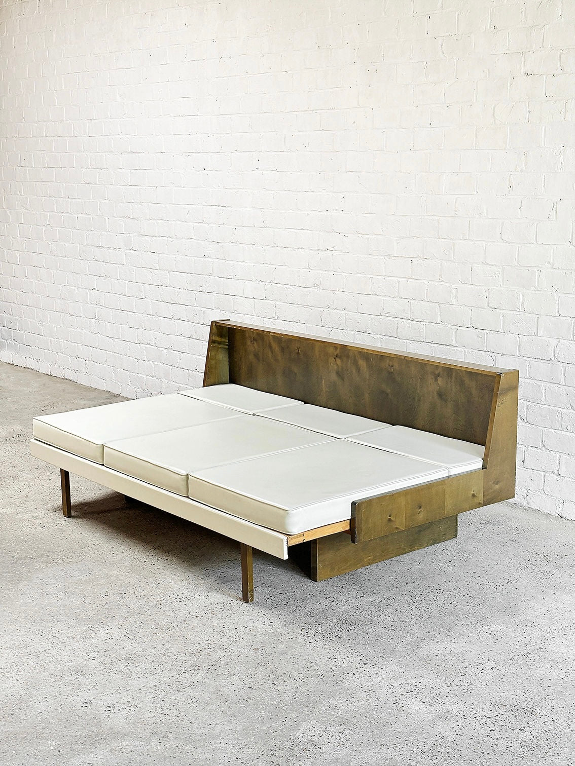 The Introverso French Modernist Sofa Set in white leather from the 1950s features a minimalist wooden frame against a textured white brick wall on a concrete floor, emphasizing clean lines and elegant simplicity.