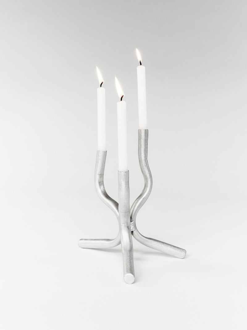 The Six Dots Design Mini Candelabra, handcrafted in a North London workshop, showcases a modern, curved design holding three lit white candles against a plain background.