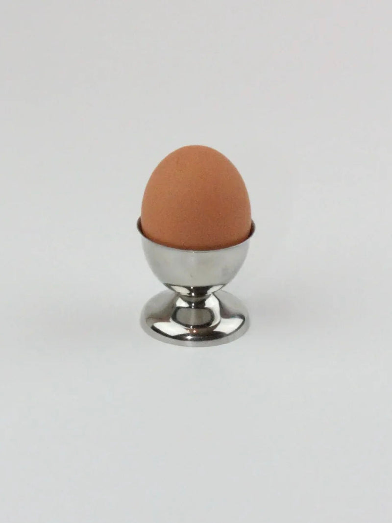 A brown egg stands upright in an elegant stainless steel egg cup from the Six Inox Egg Cups collection by Boga Avante Shop, exemplifying durability and strength against a plain white background.