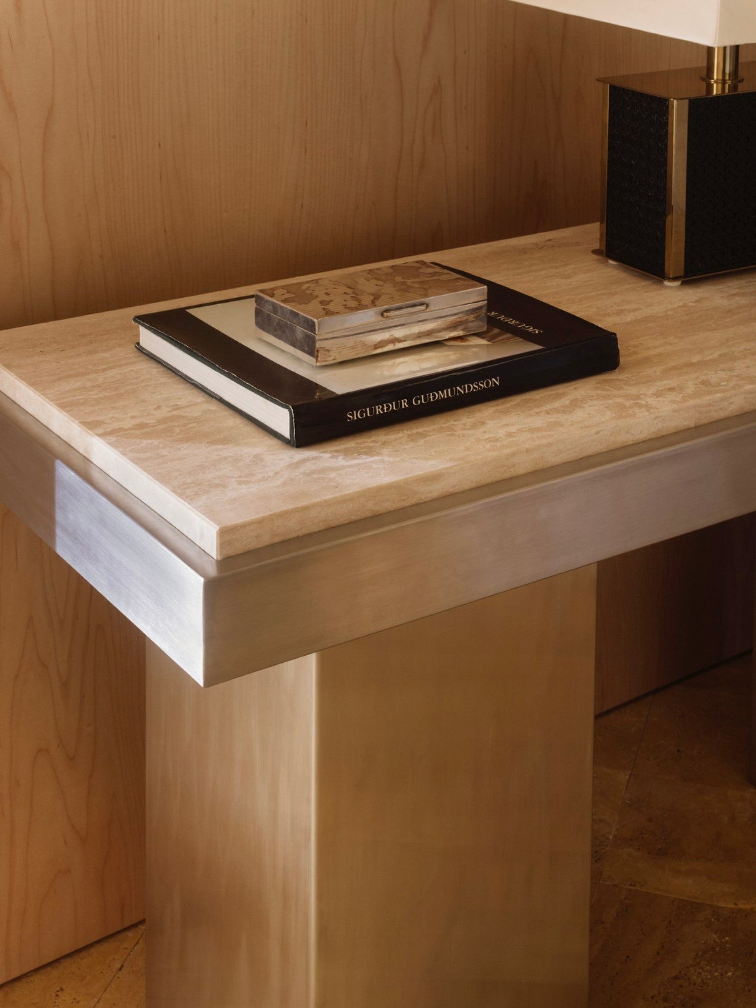 Studio Vraco's Console Table 01, featuring a brushed stainless steel base, elegantly displays two books and a metal box. Set against a wooden wall, it exemplifies Bauhaus furniture principles for a minimalist and sophisticated interior design.