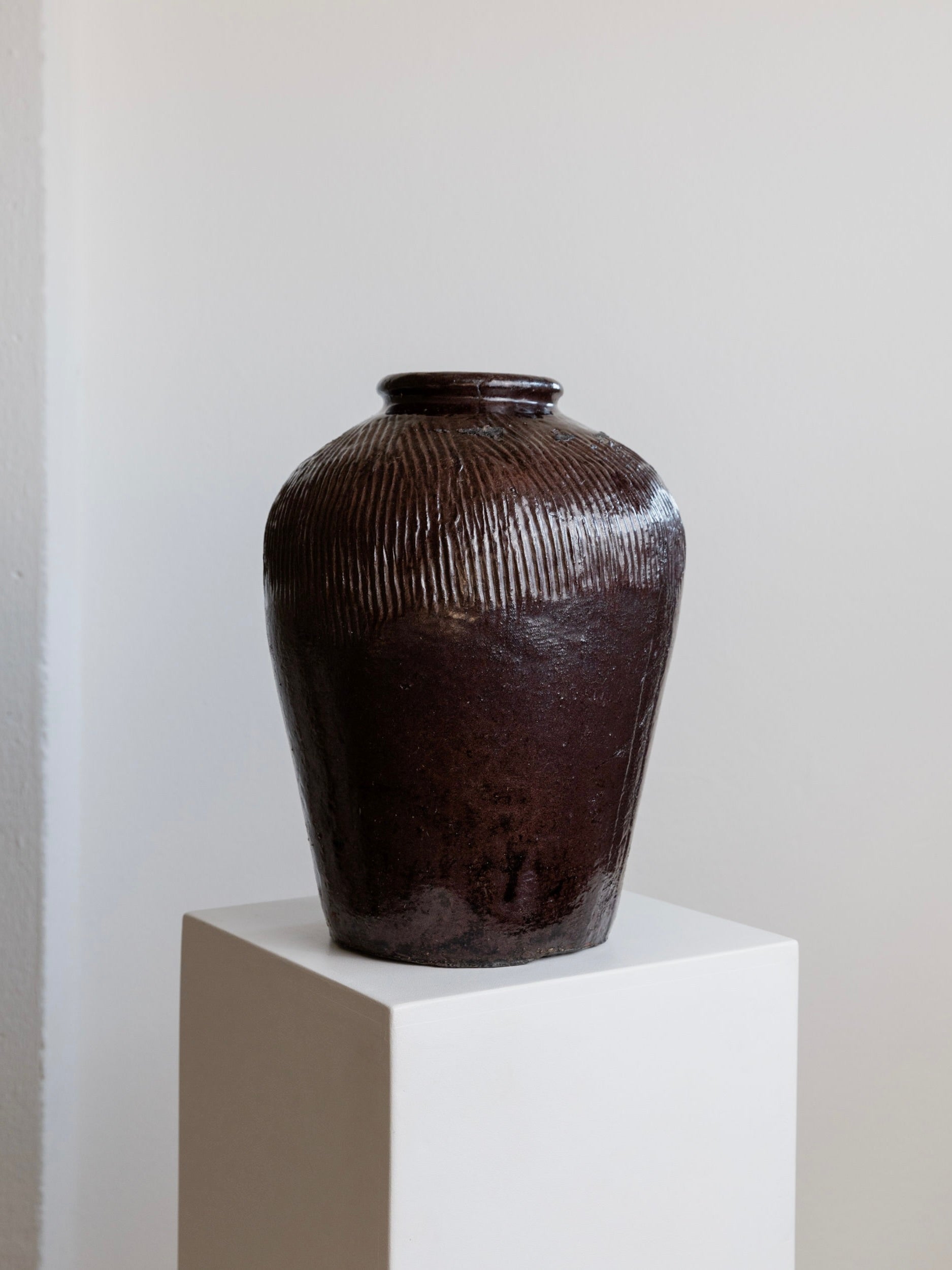 A sophisticated piece, the Antique Chinese 19th Century Ceramic by Bottega Jacobs, featuring vertical grooves and a rustic brown ceramic design, stands elegantly on a white pedestal against a light-colored background.