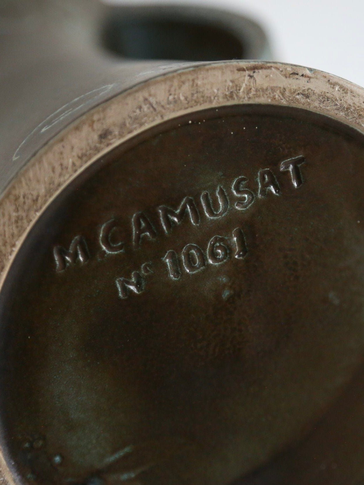 Close-up of a bronze statue's base engraved with "M. Camusat No 1061," its aged patina mirrors the vintage charm of Ancien et Jolie's 50s French Ceramic Vase, decorated with naive swirl patterns.