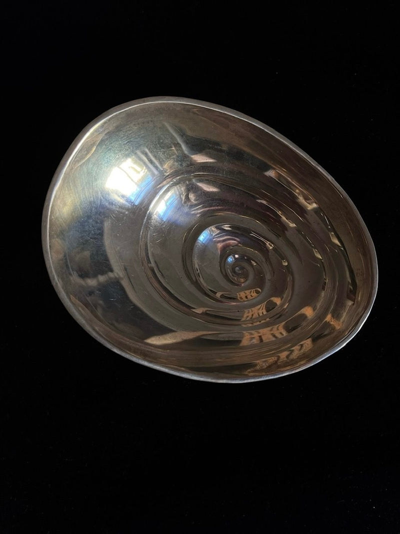A rare sterling silver Midcentury Vide-Poches by Médecine is displayed against a solid black background. The shiny, metallic bowl features an asymmetrical design with smooth, reflective surfaces and irregular contours that create a unique, modern aesthetic. Concentric patterns on the interior evoke the distinctive style of a midcentury piece by Tapio Wirkkala.