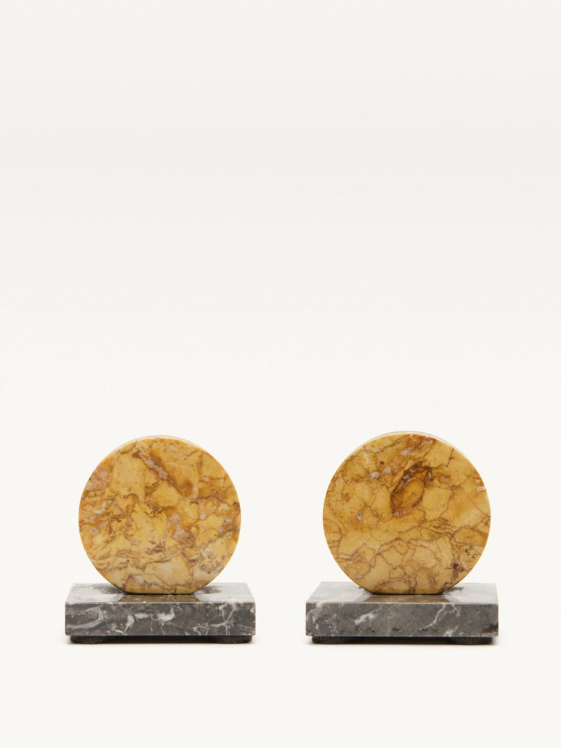 The Pair of Art Deco Marble Bookends by Galerie MLS features two circular yellow-brown marble bookends with natural patterns, each on a rectangular gray marble base, embodying the elegance of French 1930s Art Deco design against a plain background.