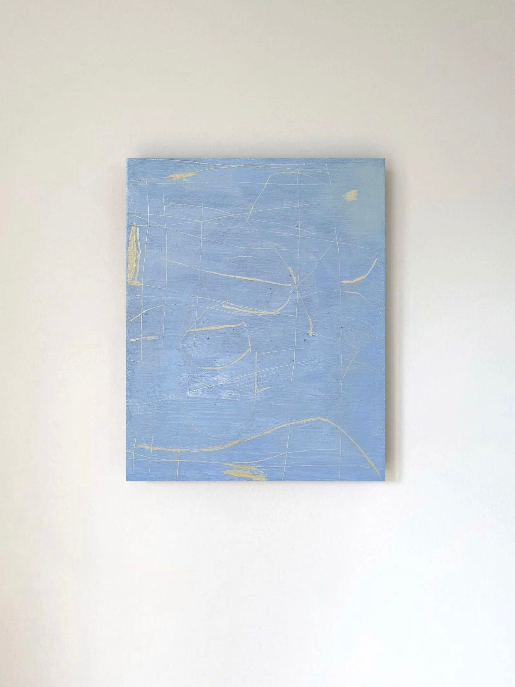 The Unsaid" by Yeliza Gevorgyan features a light blue square canvas with fine white and yellow lines, creating minimal marks. It is mounted on a plain white wall.