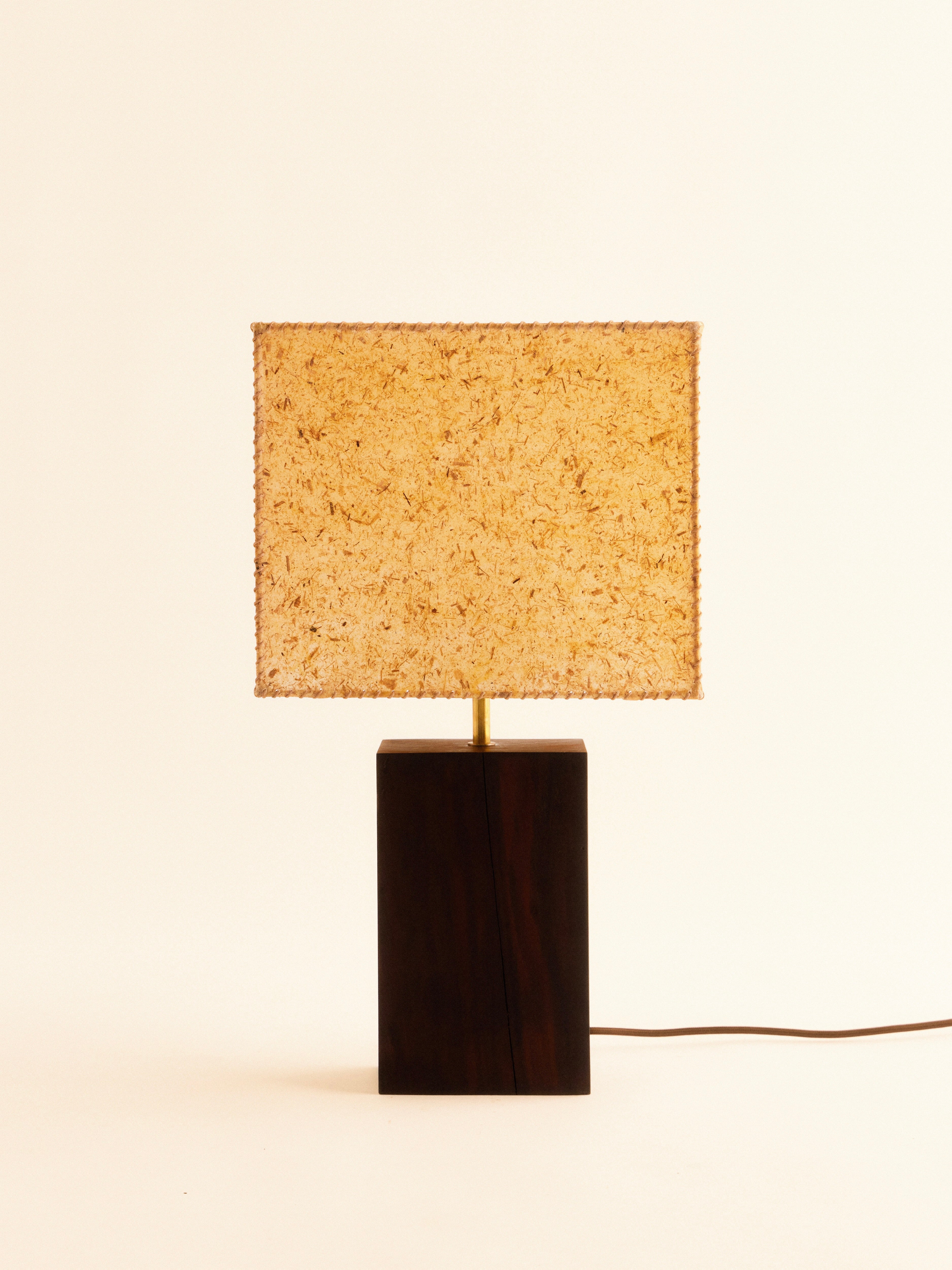 The 1948 Table Lamp by Lana Launay, handcrafted in Sydney, features a dark wooden rectangular base and is topped with a textured banana fibre square shade. Set against a plain light background, its design includes a visible power cord extending from the base.