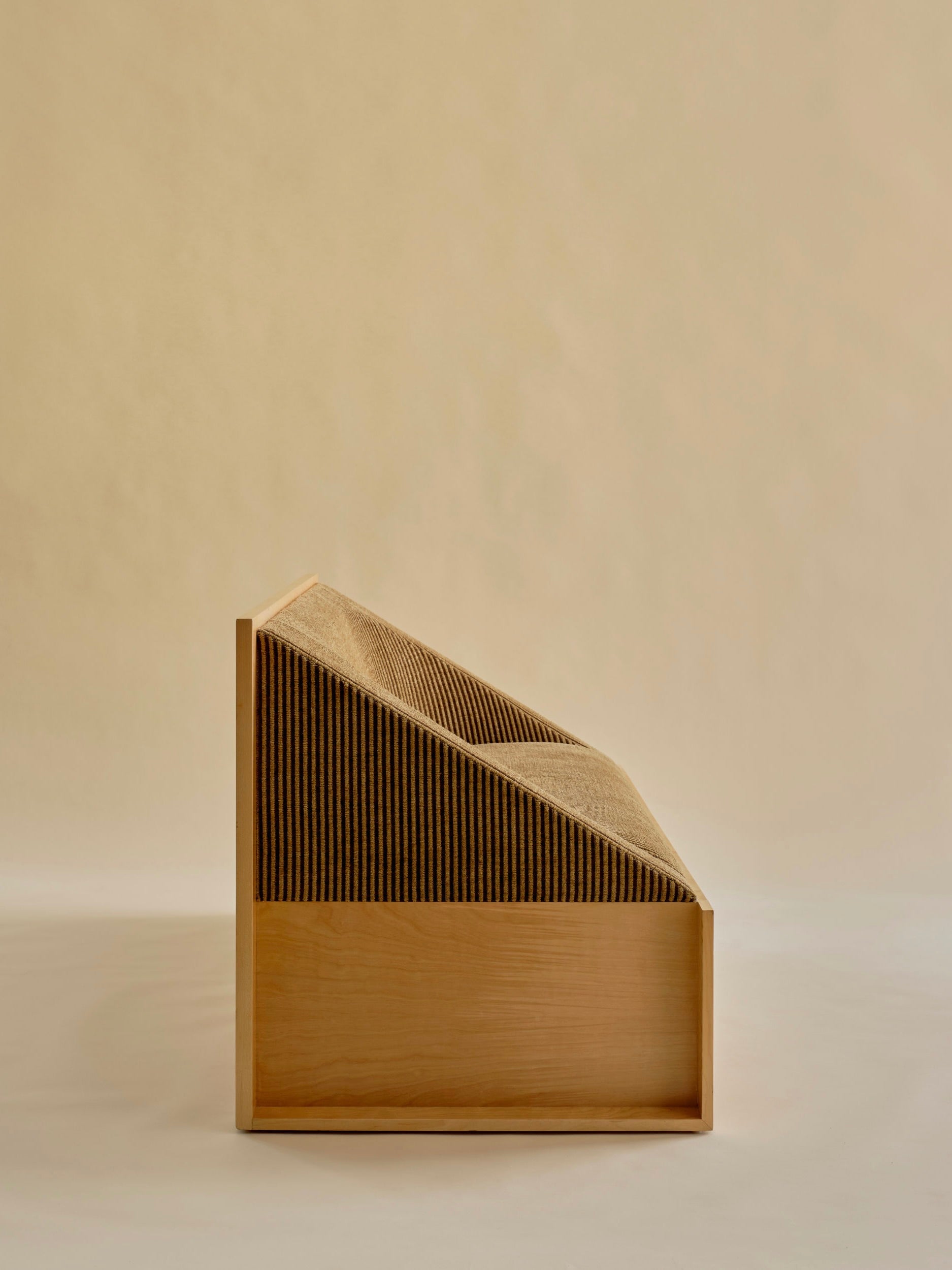 A side view of the 'Perceptions' Sofa Bench by Known Work, showcasing a modern wooden design with a unique geometric backrest and slanted corrugated texture. Its minimalist style is highlighted against a plain, neutral background.