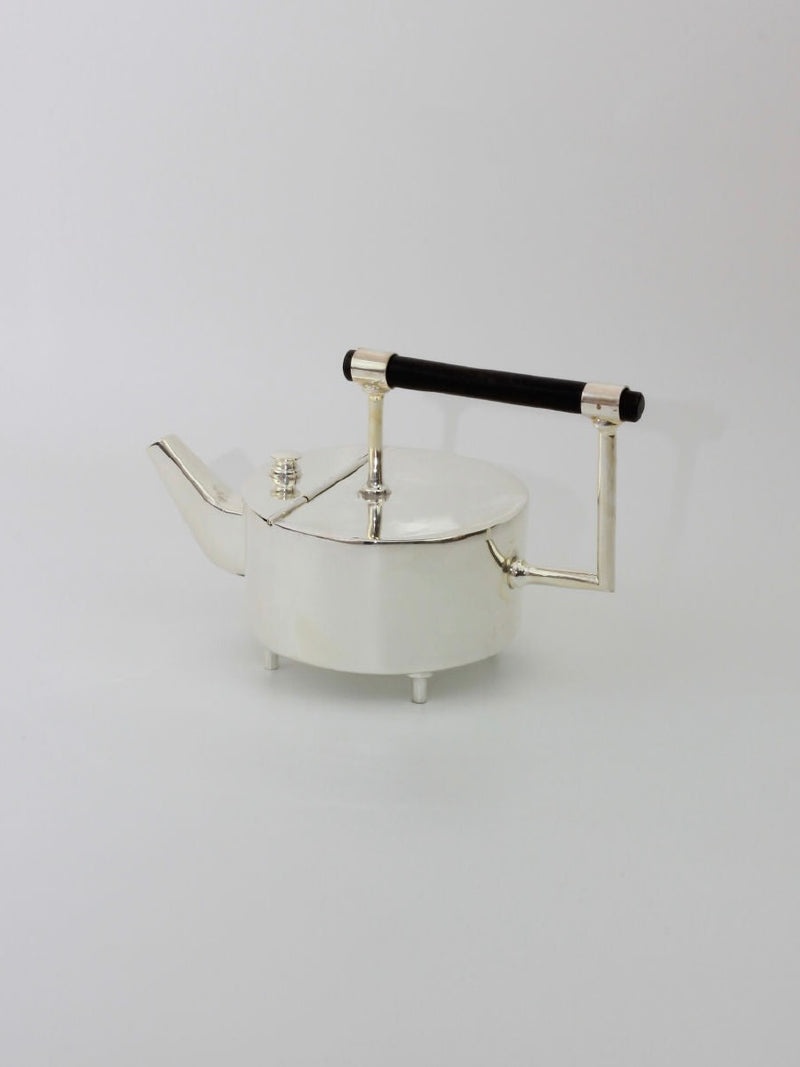 Christopher Dresser's Tea Pot from Boga Avante Shop, a modern and minimalist silver-plated teapot with a geometric design, is set against a plain white background. It features a cylindrical spout, a flat lid with a small knob, and an ebonized wood handle, embodying the innovative style of Dr. Christopher Dresser.