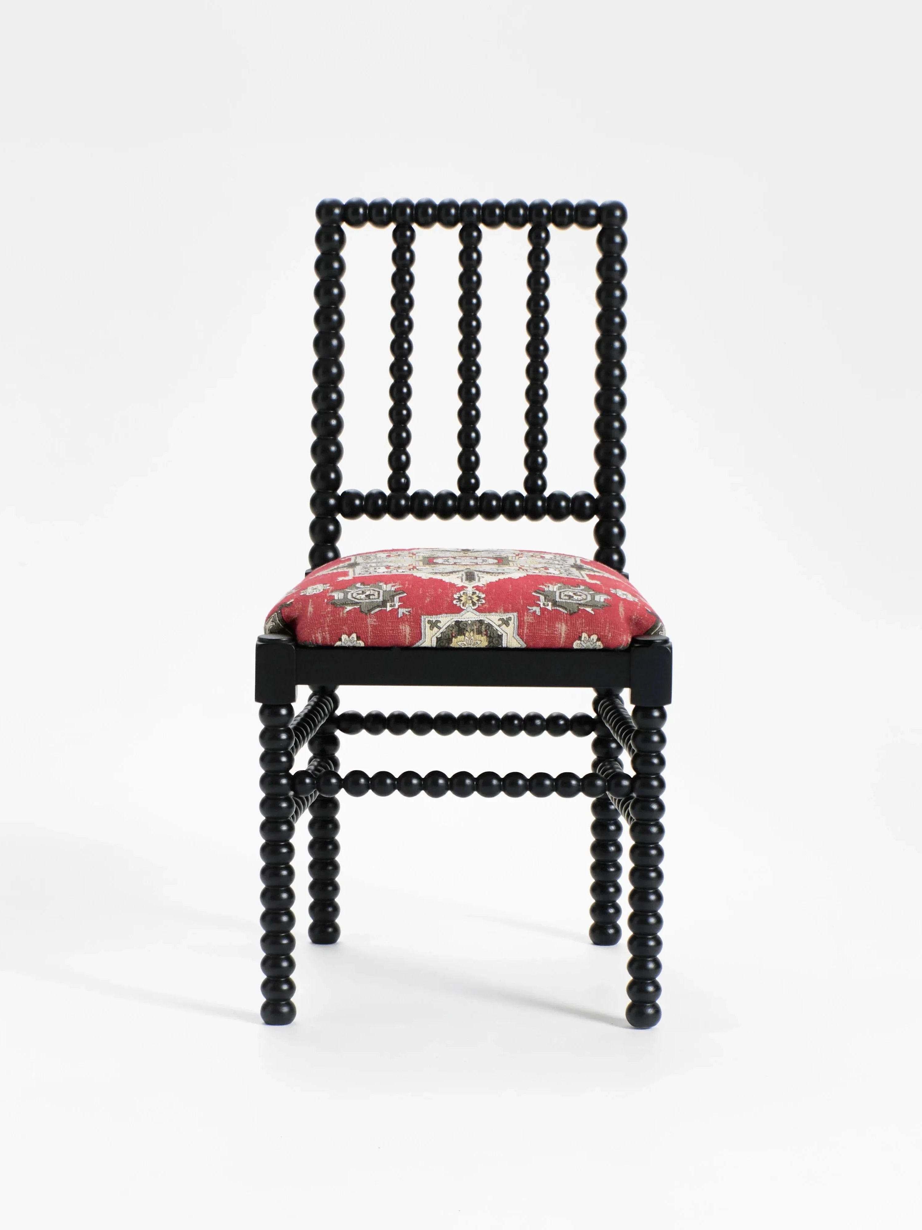 The "Bolha" Chair by Project 213A features a decorative black beaded frame with wood-turned detailing. Its cushioned seat is upholstered in luxurious red fabric with intricate light green and beige patterns on a plain white background.