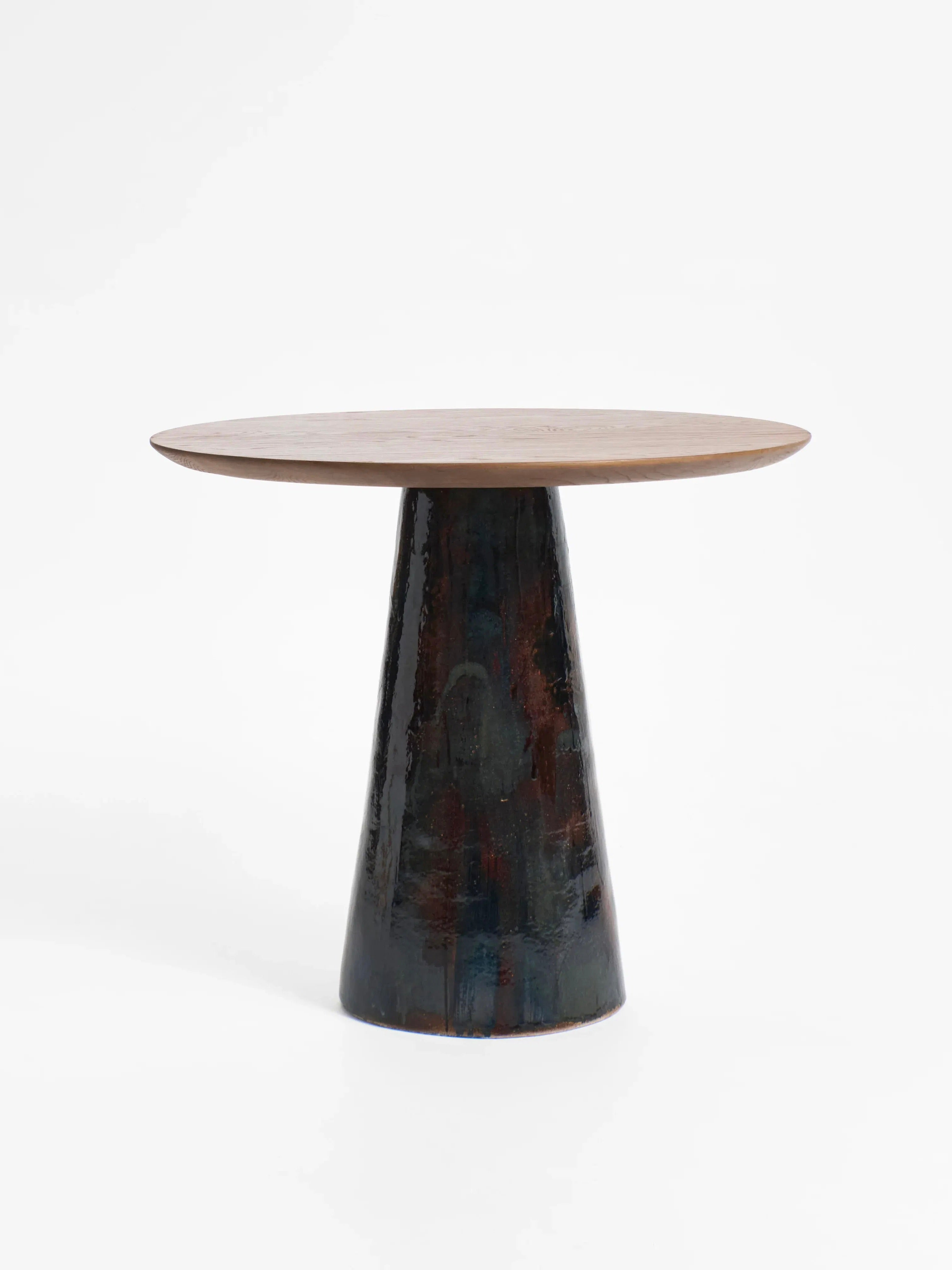 Introducing Project 213A's Porto Belo Table: this modern round wood table features a smooth, light-colored top and a dark, textured pedestal base. Reminiscent of hand-sculpted ceramic against a white backdrop, it adds sleek elegance to any bistro dining setting.